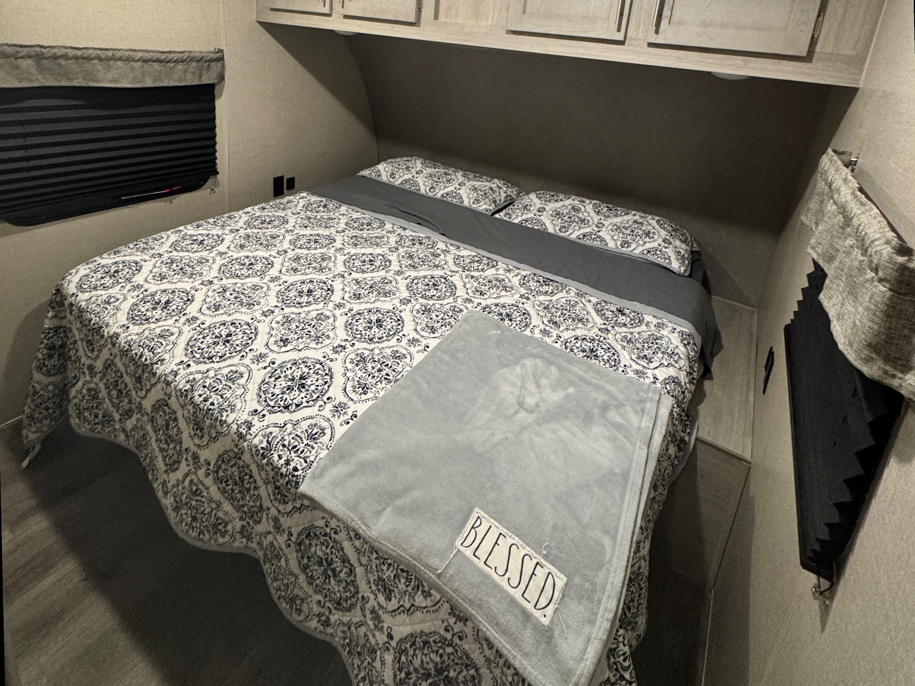 Comfortable RV rental bedroom featuring a bed with patterned linens, overhead storage, and privacy blinds on windows.. Coachmen Catalina 2022