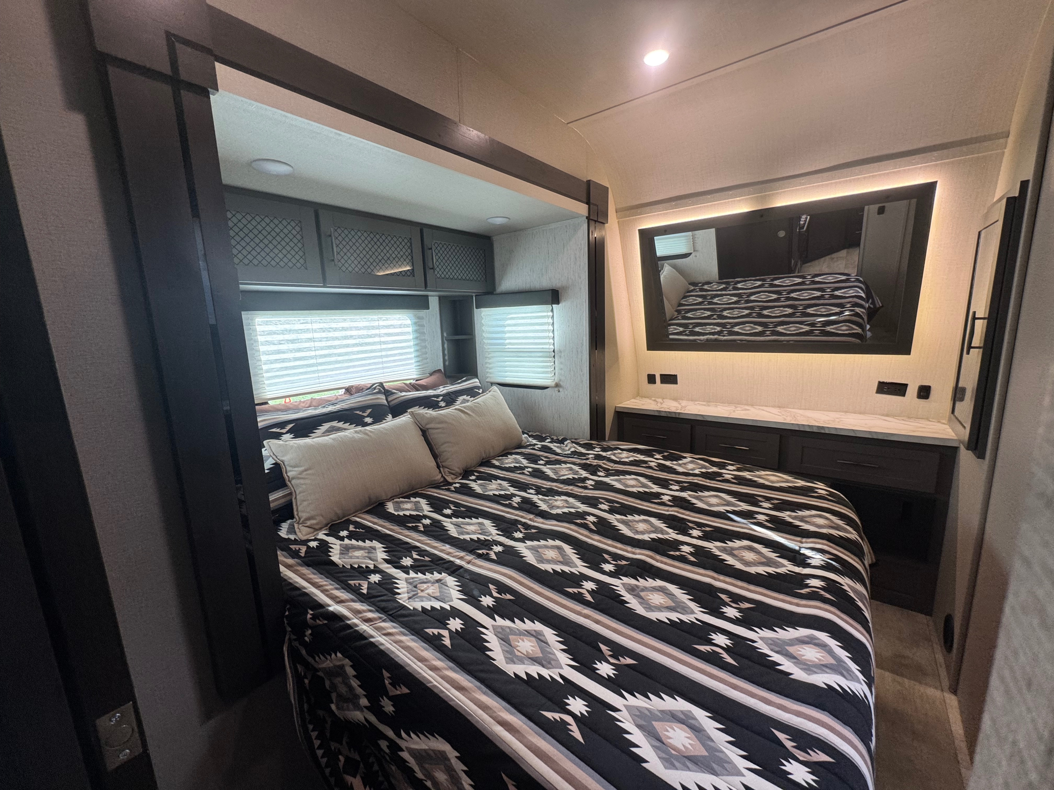 Cozy RV rental bedroom with Southwestern quilt, overhead storage, and a modern lighted vanity.. Grand Design Momentum 2022