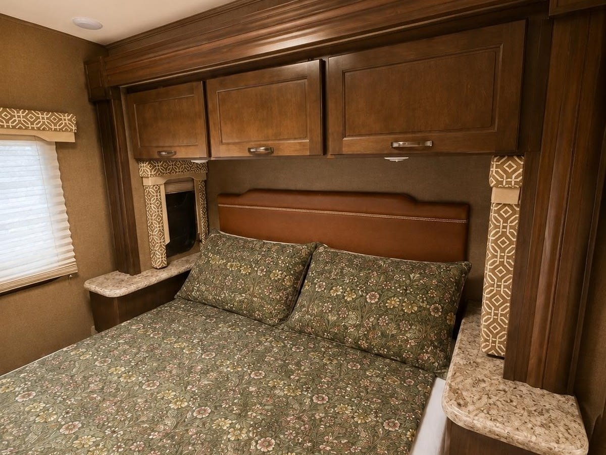 This RV rental's cozy bedroom features a bed with floral bedding, wood cabinets, and a window for comfort.. Thor Freedom Elite 2018