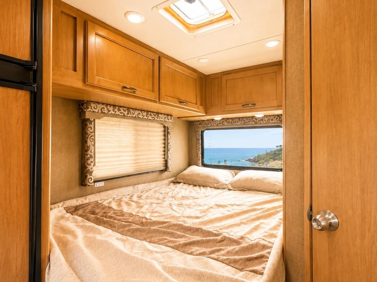 Cozy RV rental bedroom with a stunning ocean view, featuring a comfortable bed, wooden cabinets, and a ceiling light.. Thor Four Winds 2018