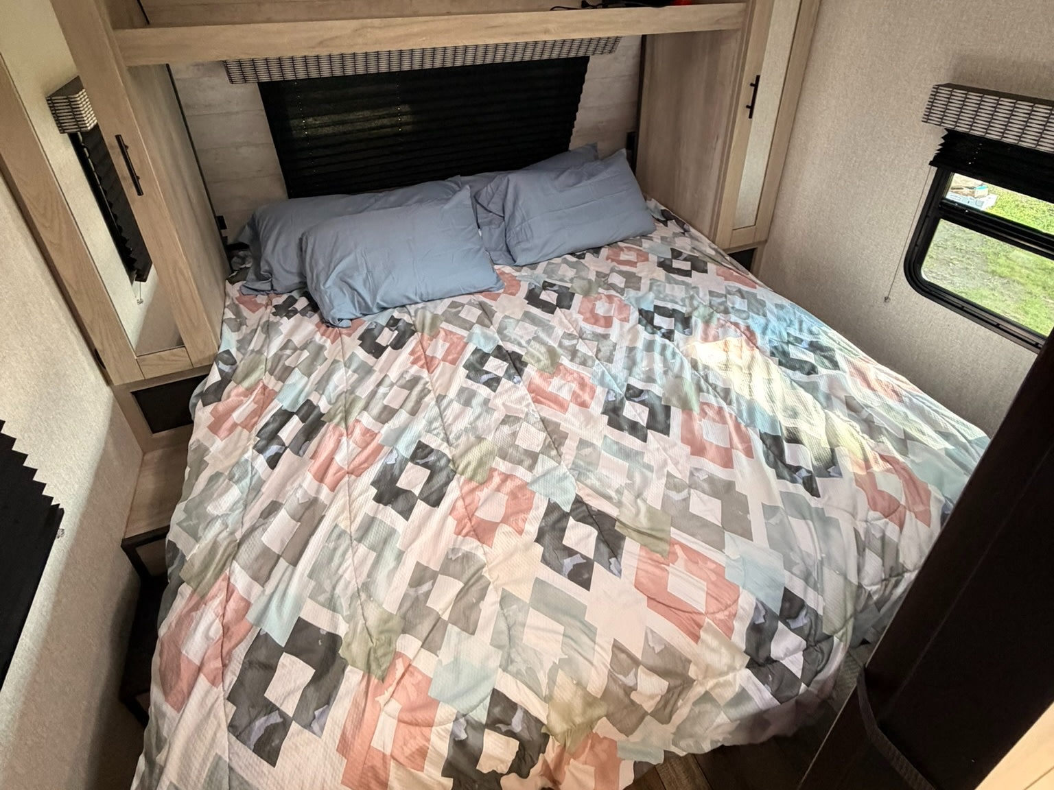 An RV rental's cozy bedroom features a geometric patterned comforter, blue pillows, and natural light from the window.. KZ Connect 2022