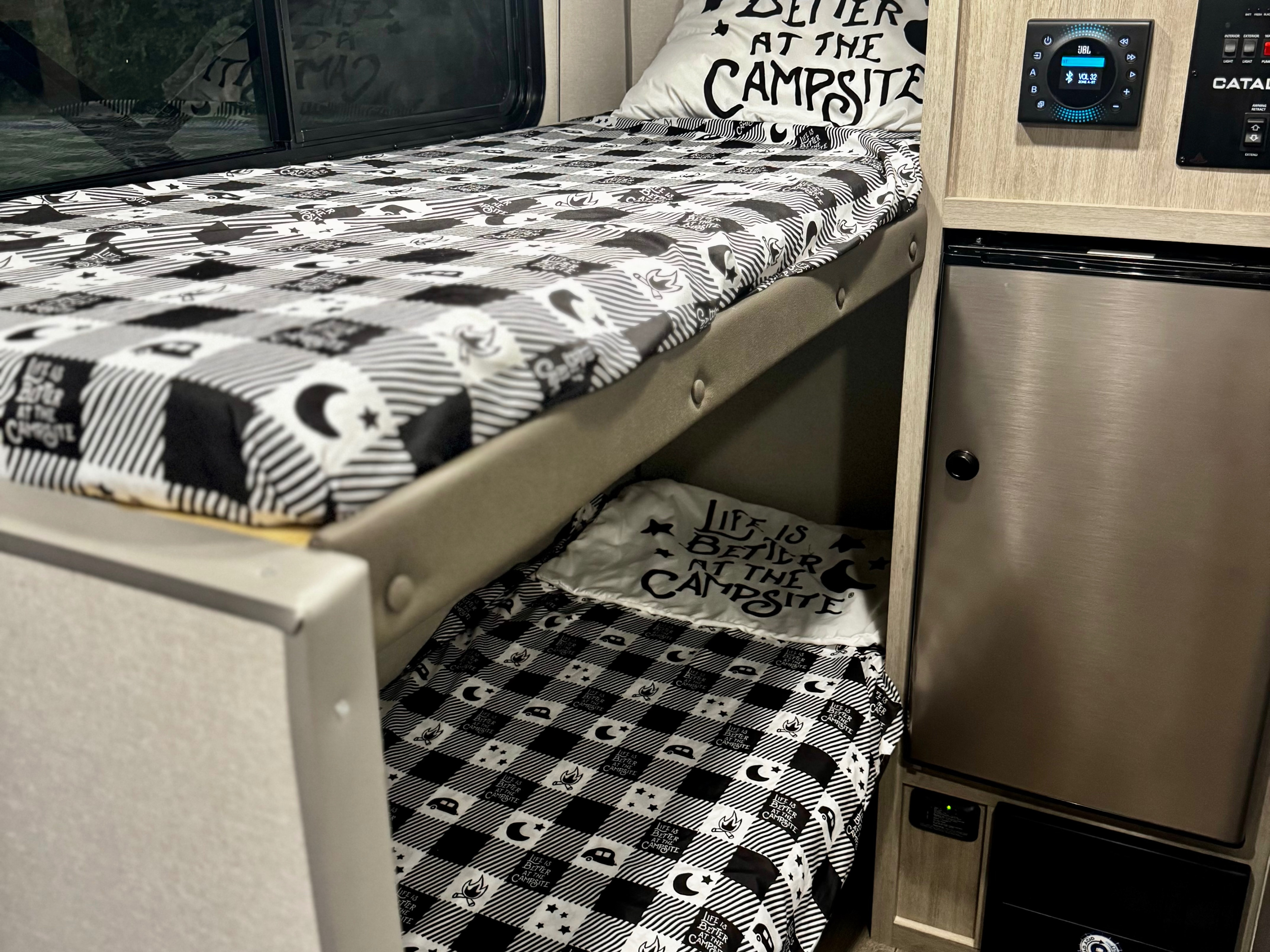 Cozy RV rental bunk beds with "Life is better at the campsite" bedding, alongside a JBL control panel and compact fridge.. Coachmen Catalina Summit Series 134BHX 2025