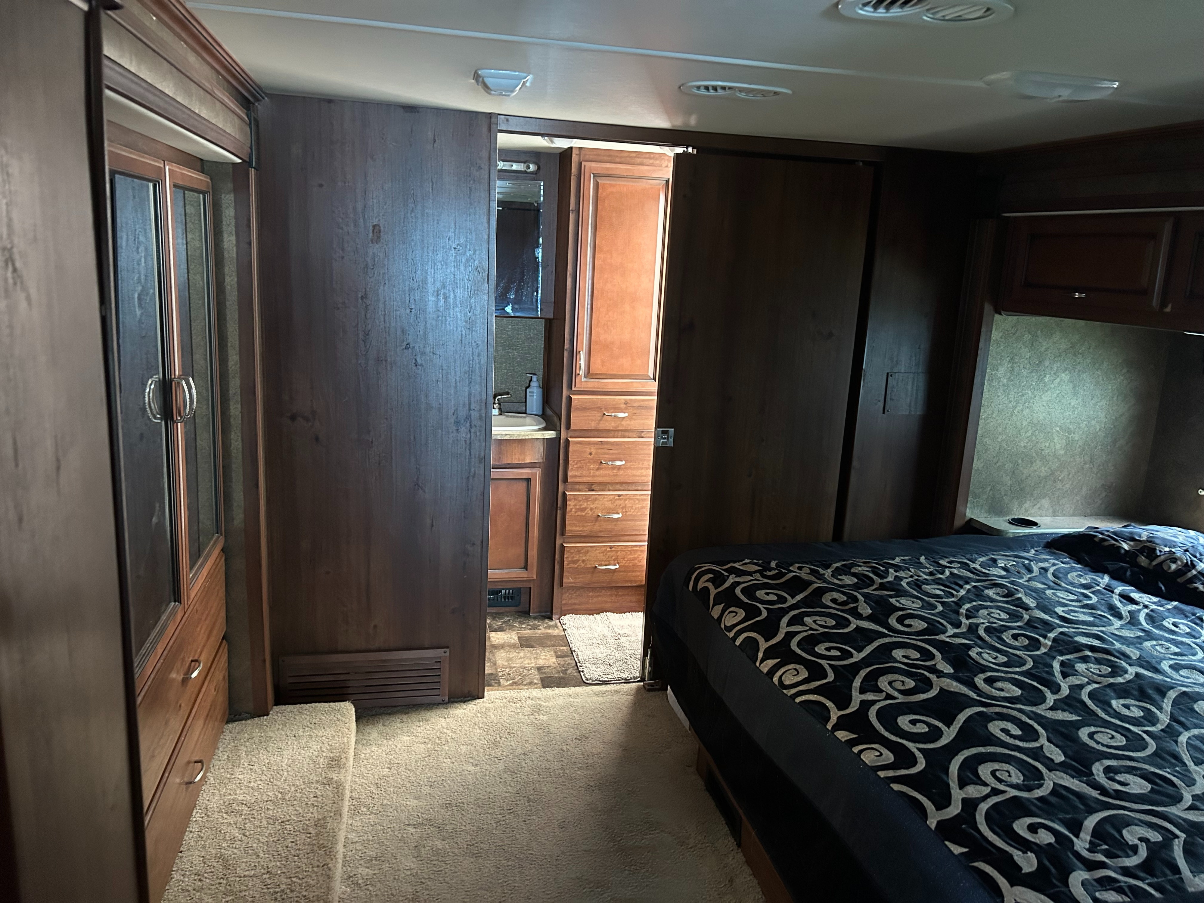 RV rental interior: bedroom with a patterned bed & wardrobe, and a partial view into the compact bathroom with a sink.. Bounder Classic 2014