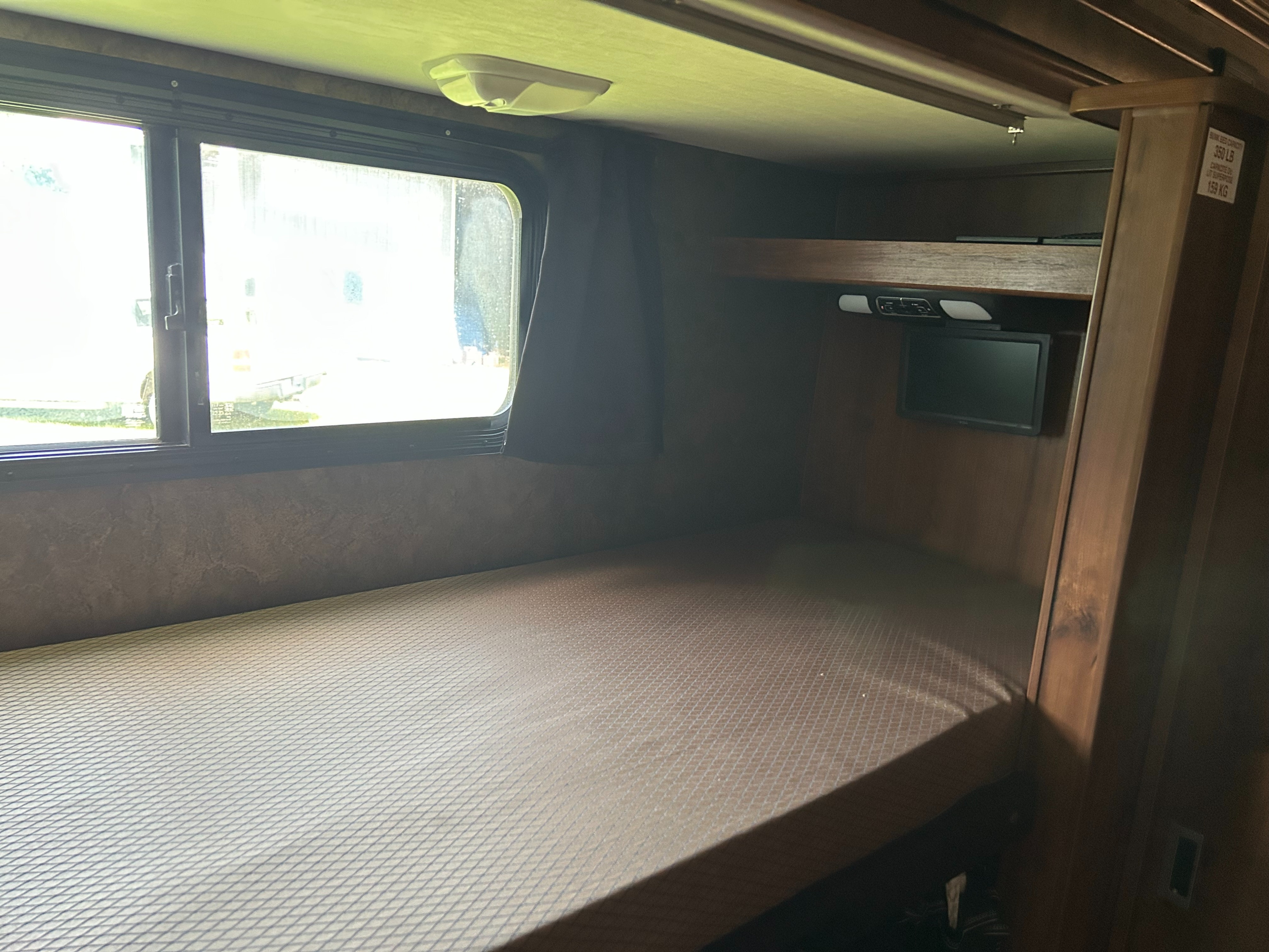 Inside an RV rental, a cozy bunk bed with a large window and built-in TV, perfect for relaxing after travel.. Bounder Classic 2014