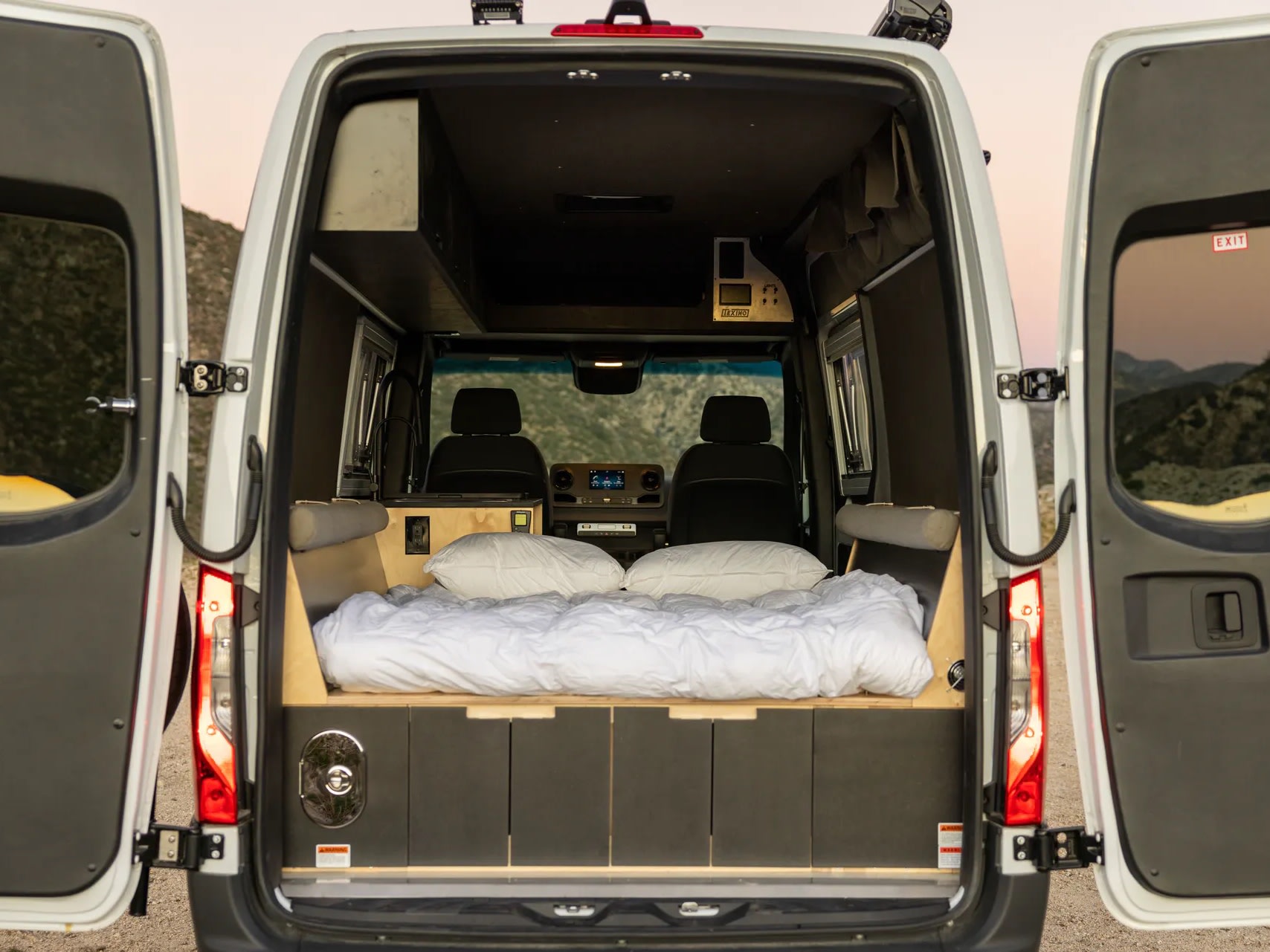Cozy rv rental camper van interior, seen from open rear doors. Features a comfortable bed, storage, and front seats for travel.. Mercedes Sprinter 2021