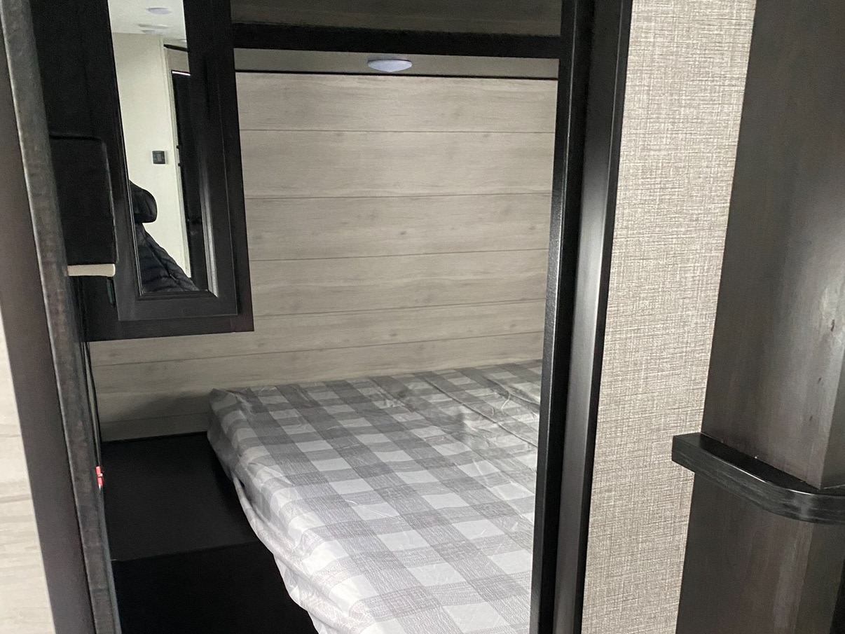 RV rental bedroom: a compact sleeping area featuring a plaid bed, light wood wall paneling, and a framed mirror.. Jayco Jay Flight SLX 2022