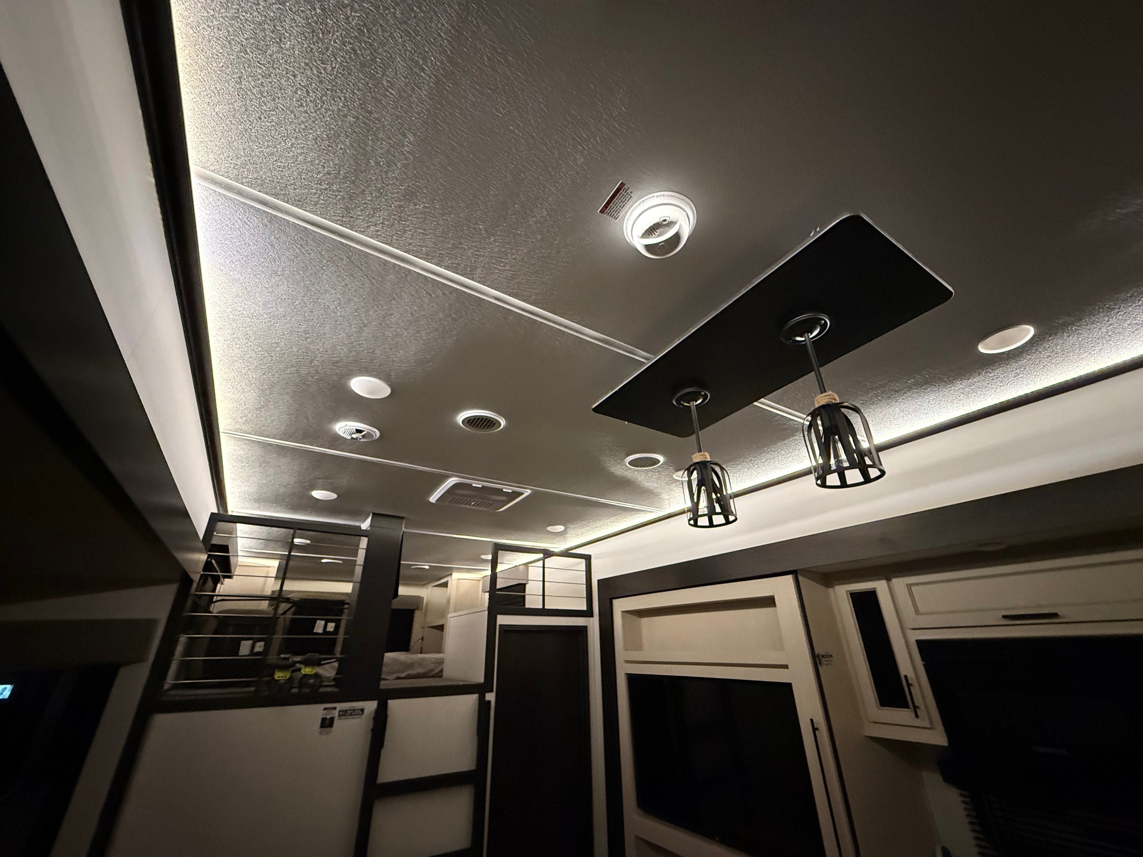 Interior of an RV rental, featuring a modern ceiling with various lights, a cozy bunk loft, and sleek cabinetry.. Forest River Sabre - 36DBB 2027