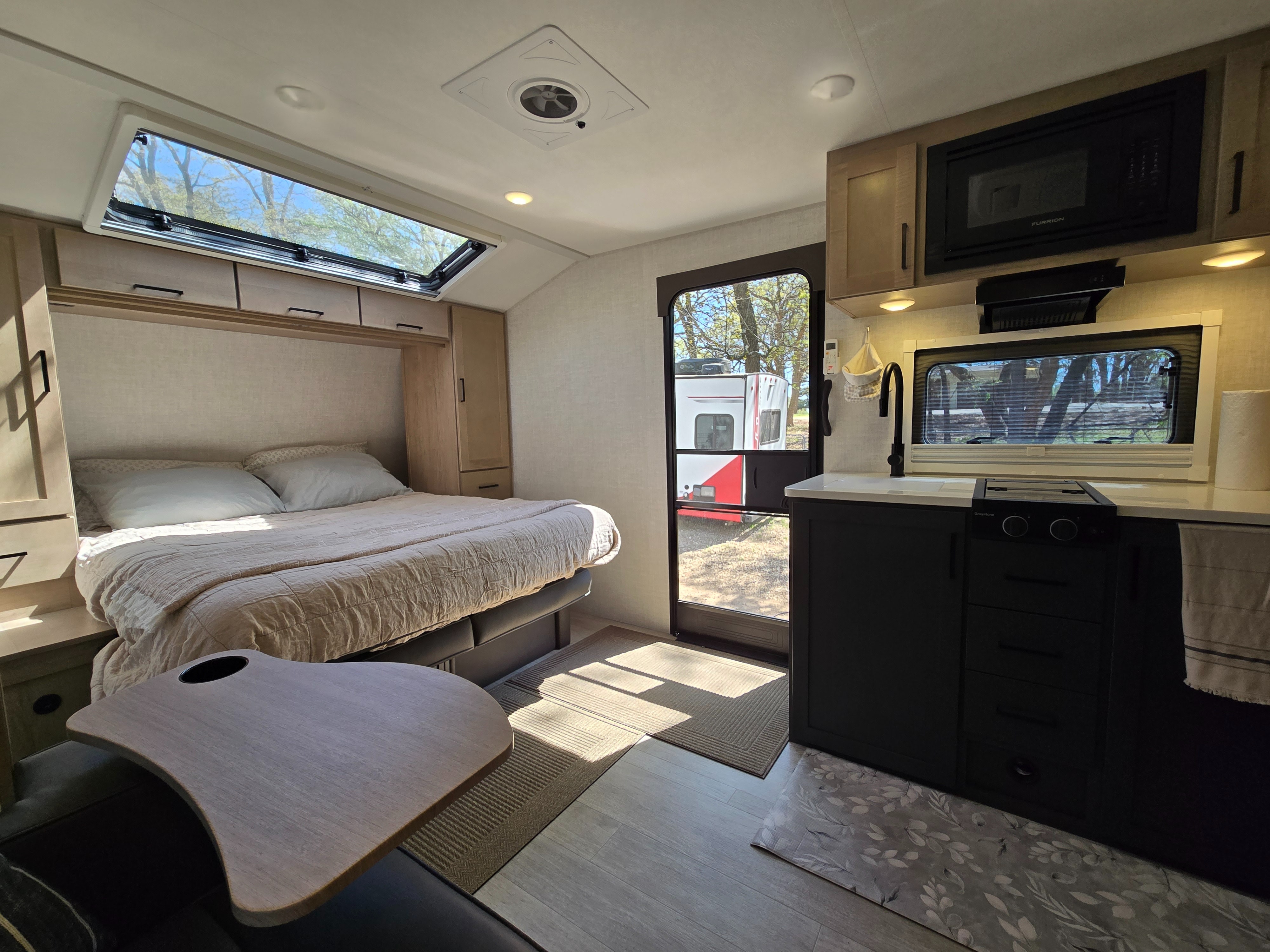 Inside a stylish RV rental, offering a cozy bed, a compact kitchen with microwave, and serene outdoor views.. Ember OVERLAND / 221MSL 2026