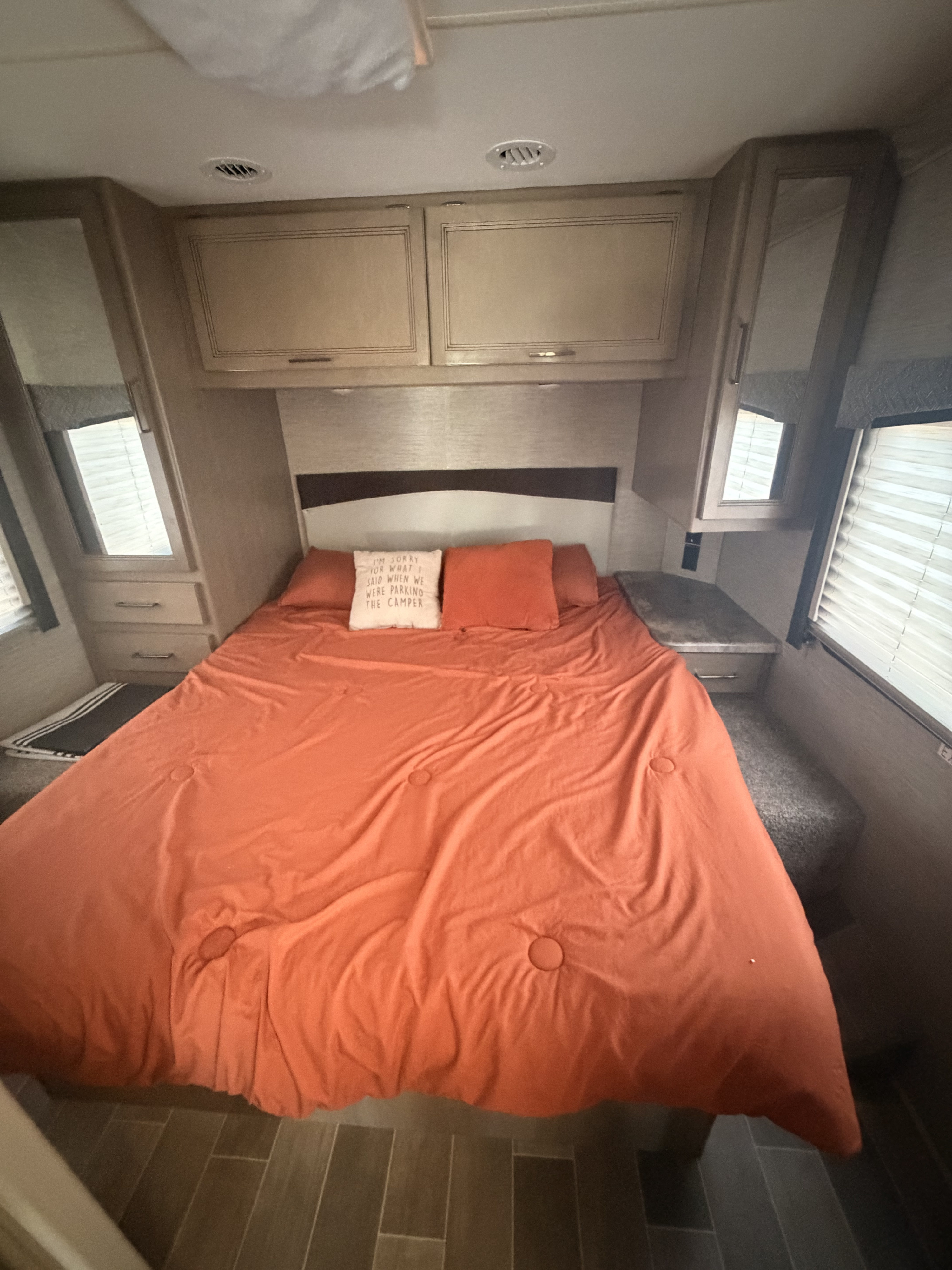 This rv rental features a cozy bedroom with an orange bed, overhead cabinets, and windows on both sides.. Thor Chateau 2022