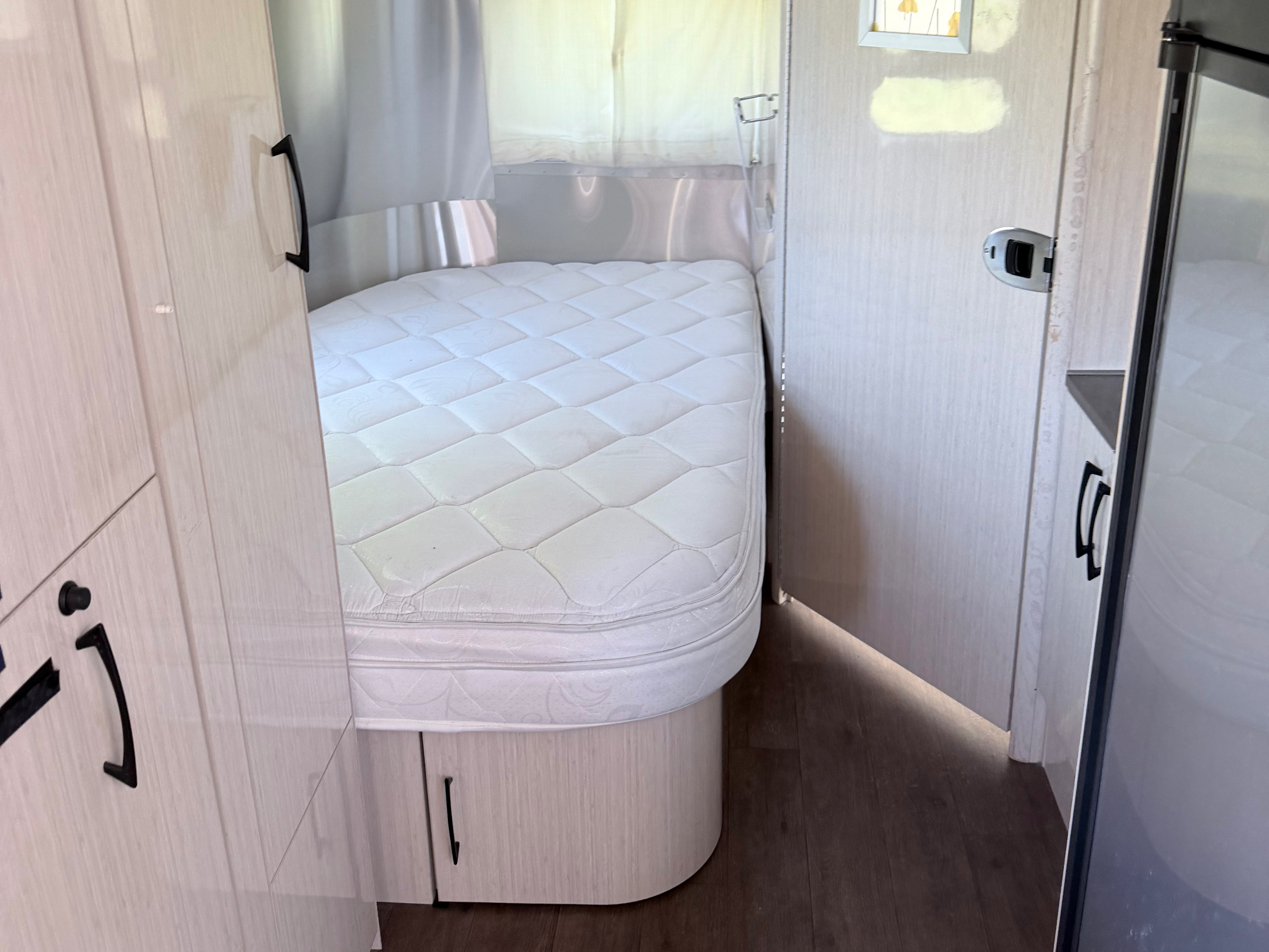Inside this RV rental: a compact bedroom with a white mattress, sleek wooden cabinets, and signature curved walls.. Airstream International 2015