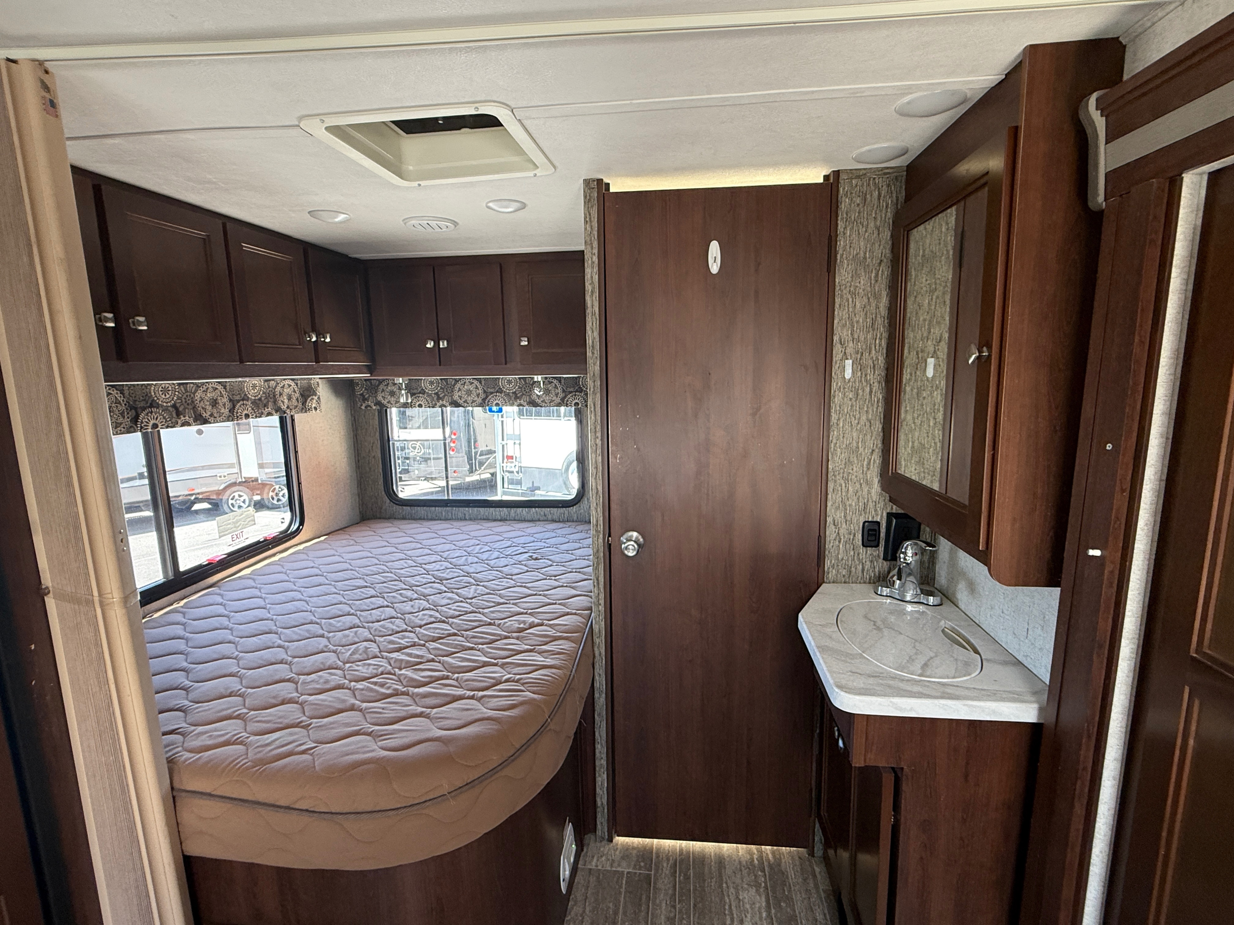 RV rental interior with a cozy bedroom featuring a bed and overhead cabinets, plus a compact bathroom vanity.. Forest River Sunseeker MBS 2018