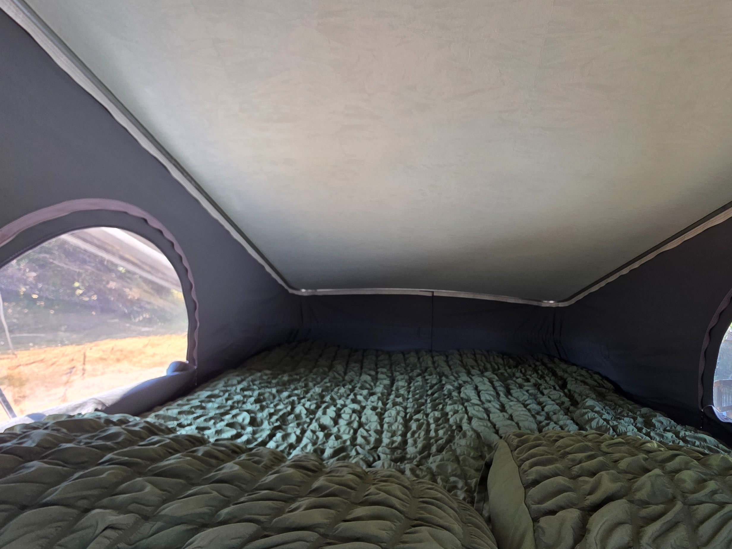 An rv rental pop-top camper's cozy sleeping area, featuring a quilted green mattress and a side window view.. Winnebago Porto 2021