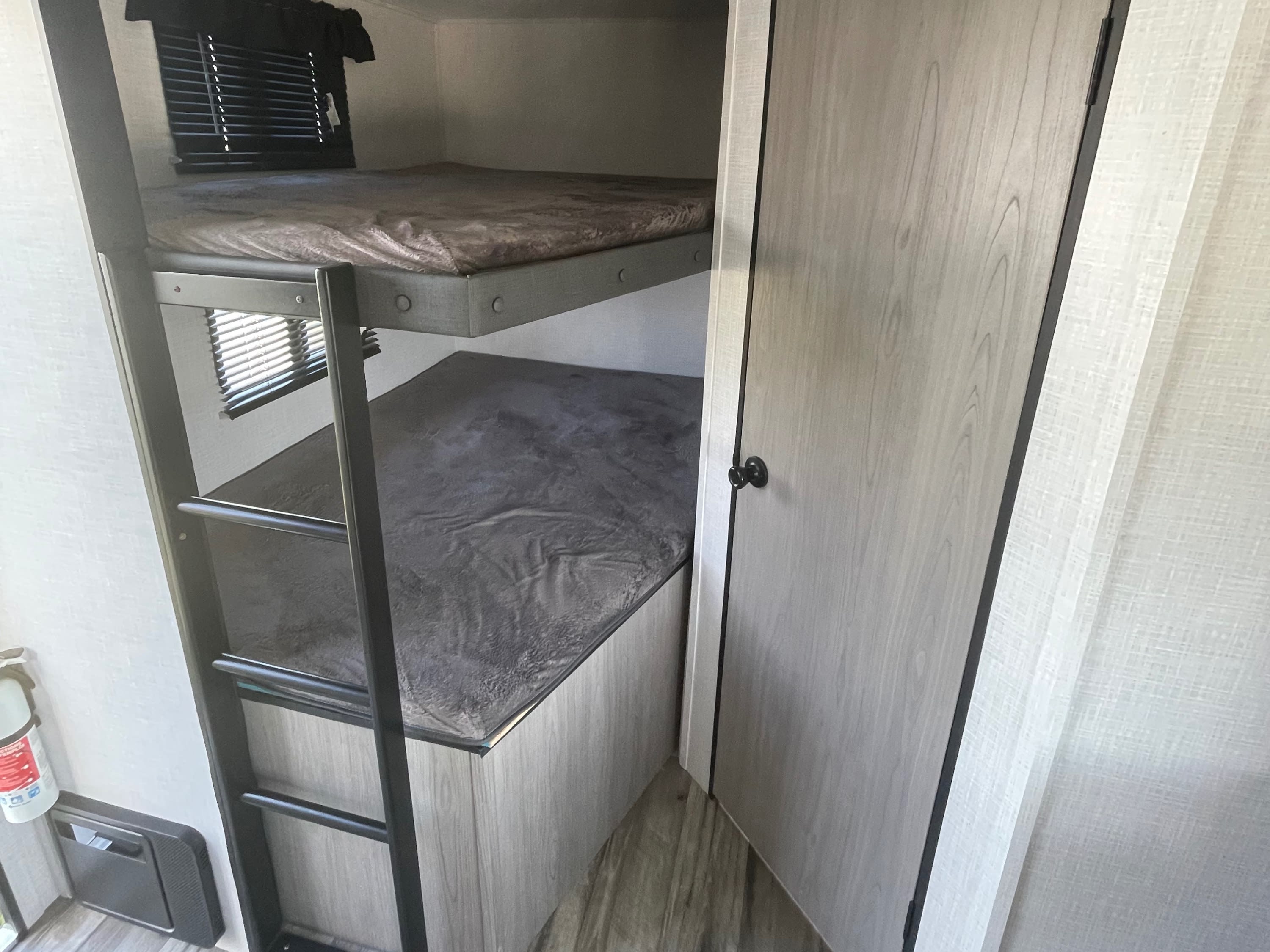 Inside this RV rental: modern bunk beds with a ladder provide comfortable sleeping. A door is on the right.. Dutchmen Coleman Light 2022