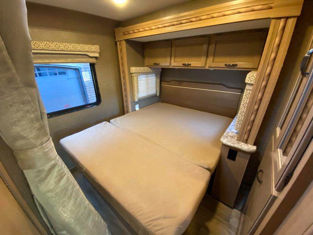 RV rental bedroom: A comfortable, large bed with overhead cabinets, a side window, and decorative trim details.. Thor Freedom Elite 2022