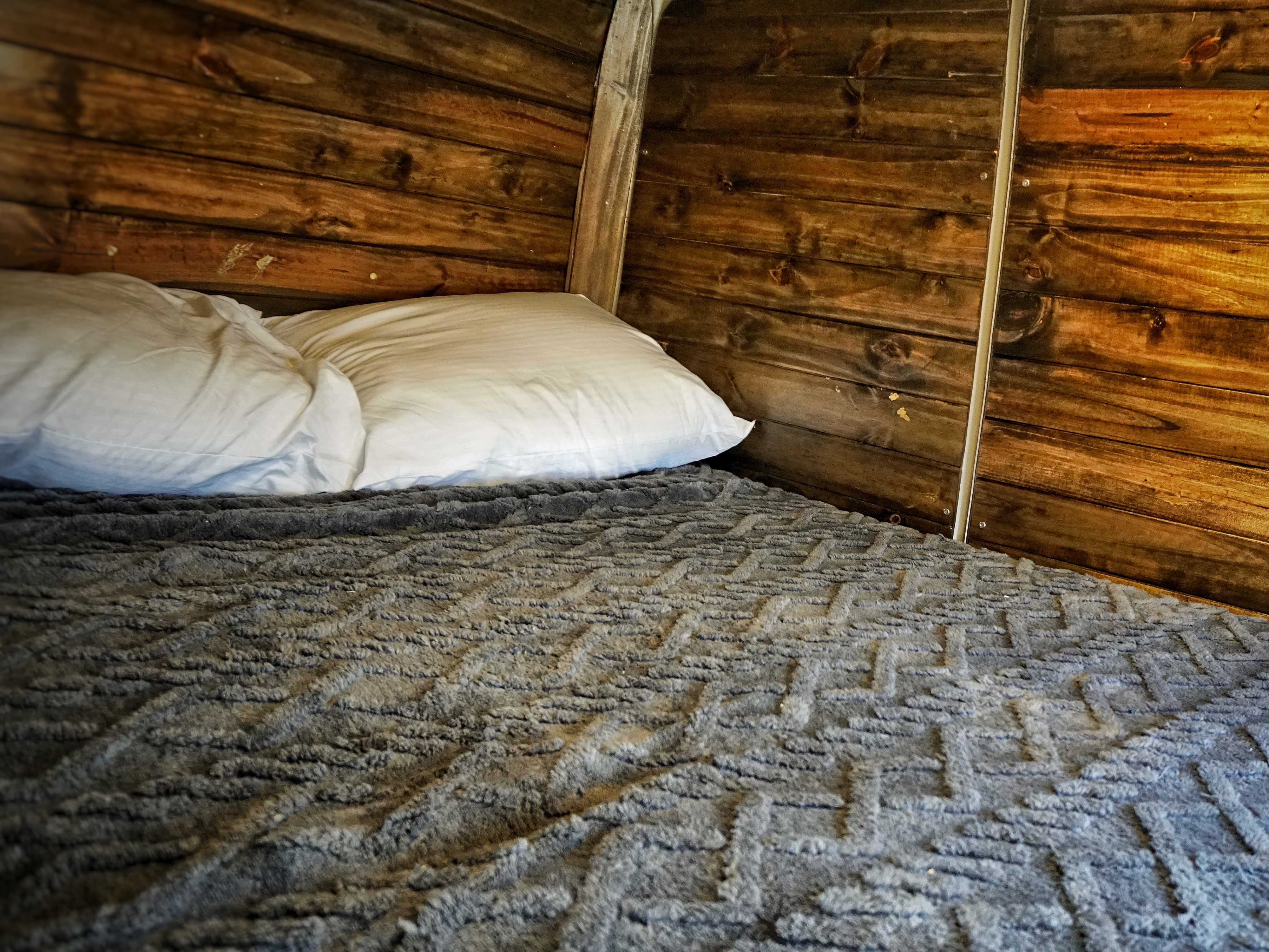 Cozy sleeping area in an RV rental, featuring a bed with white pillows, a grey textured blanket, and rustic wooden walls.. Dodge Sprinter 2006