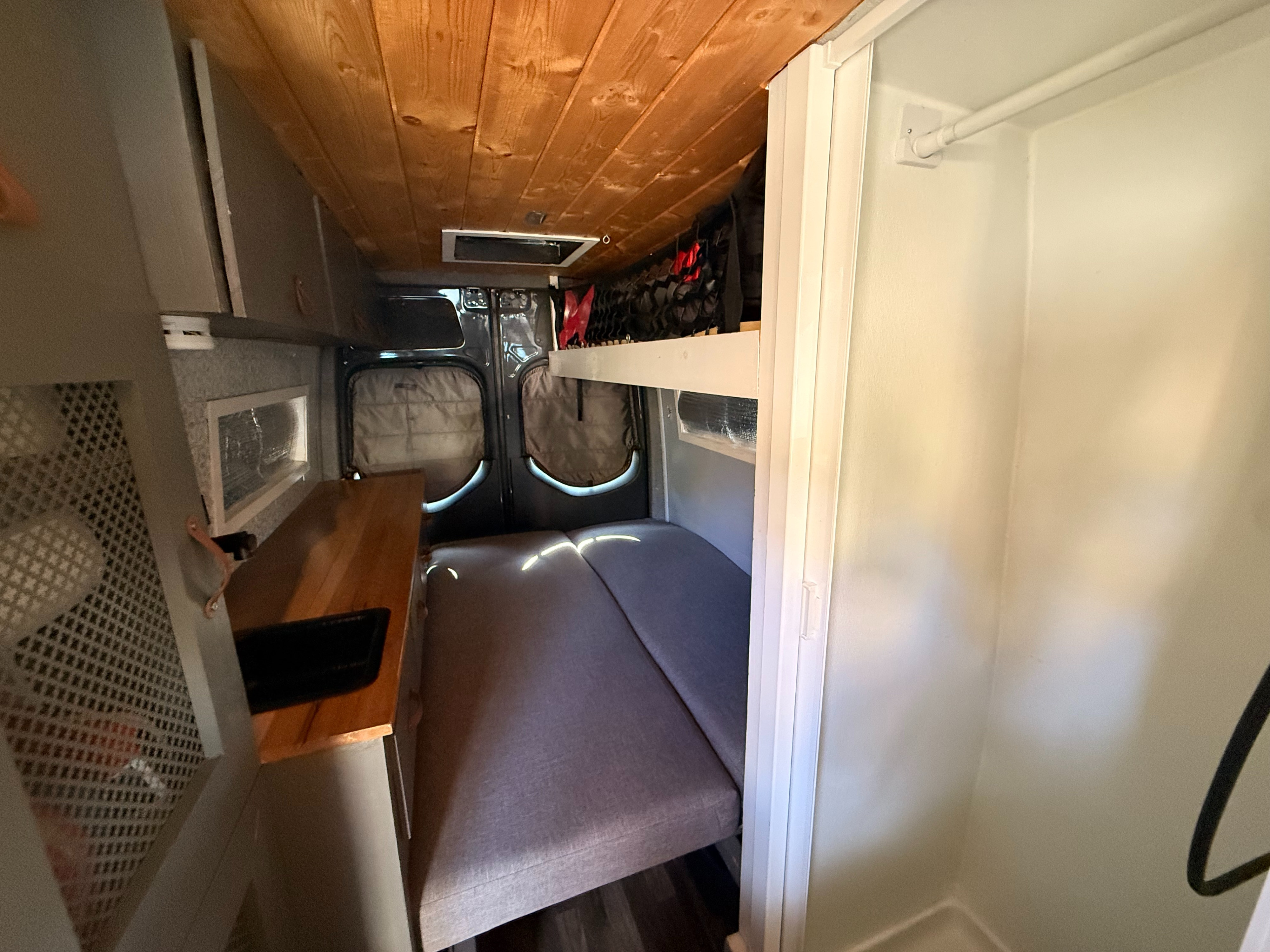 This rv rental interior offers a bed with overhead storage, a small counter, and a compact shower area on the right.. Mercedes-Benz Sprinter 2021