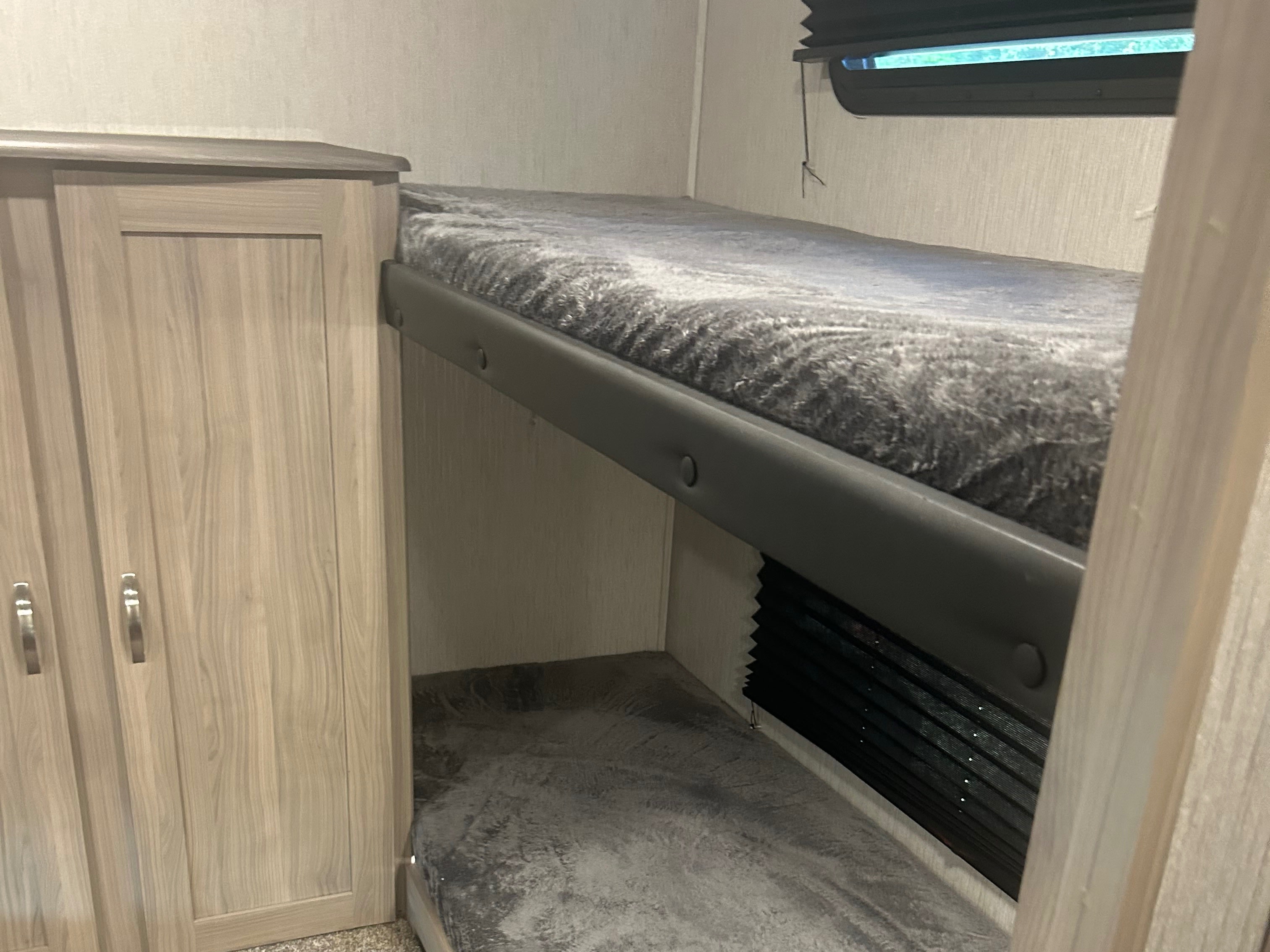 An RV rental features cozy bunk beds with fuzzy gray blankets and an adjacent light-colored wood wardrobe for storage.. Coachmen Freedom Express 2021