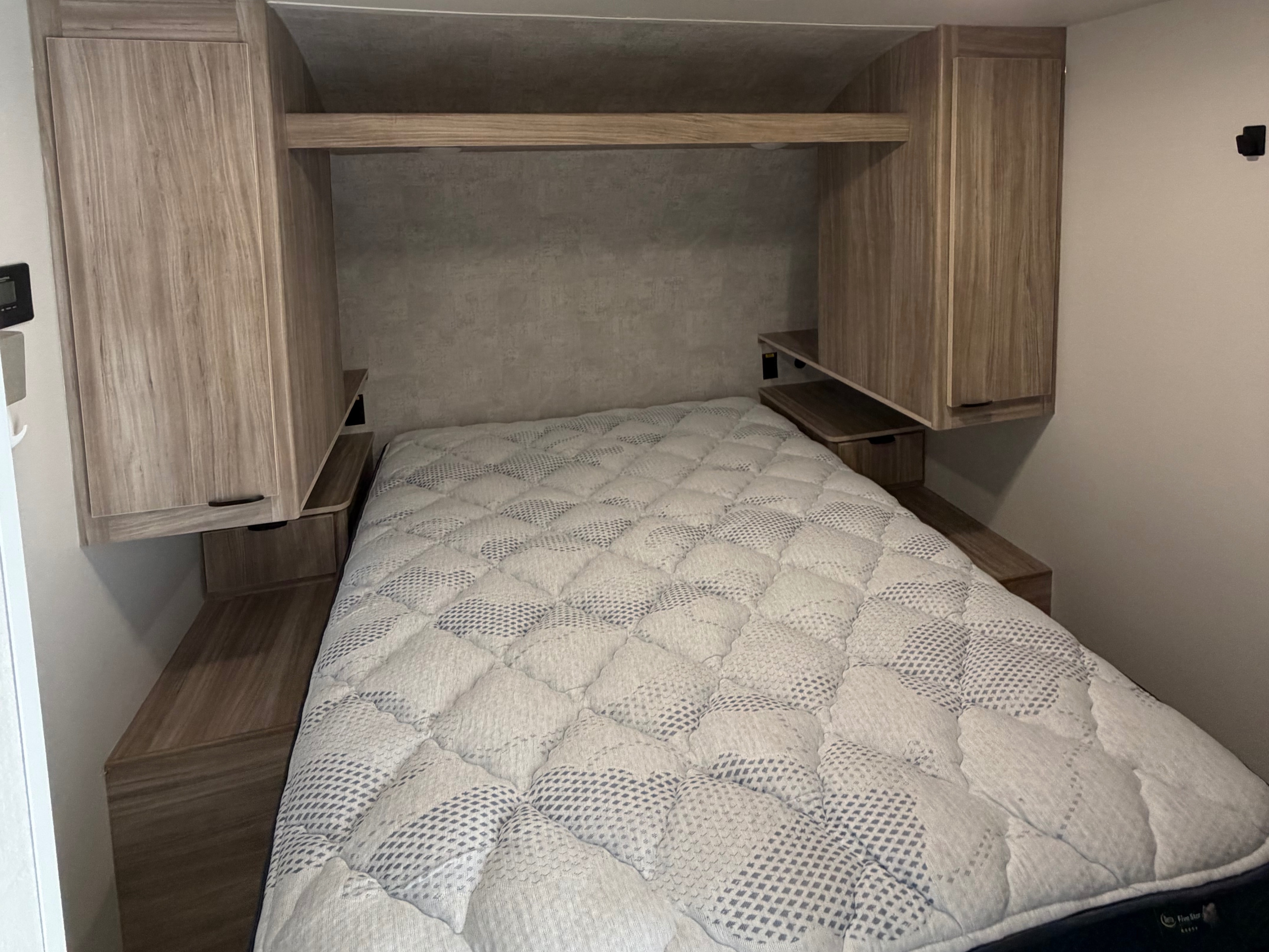 RV rental bedroom featuring a mattress, overhead cabinets, and integrated side shelves for convenient storage.. Winnebago Access 2025