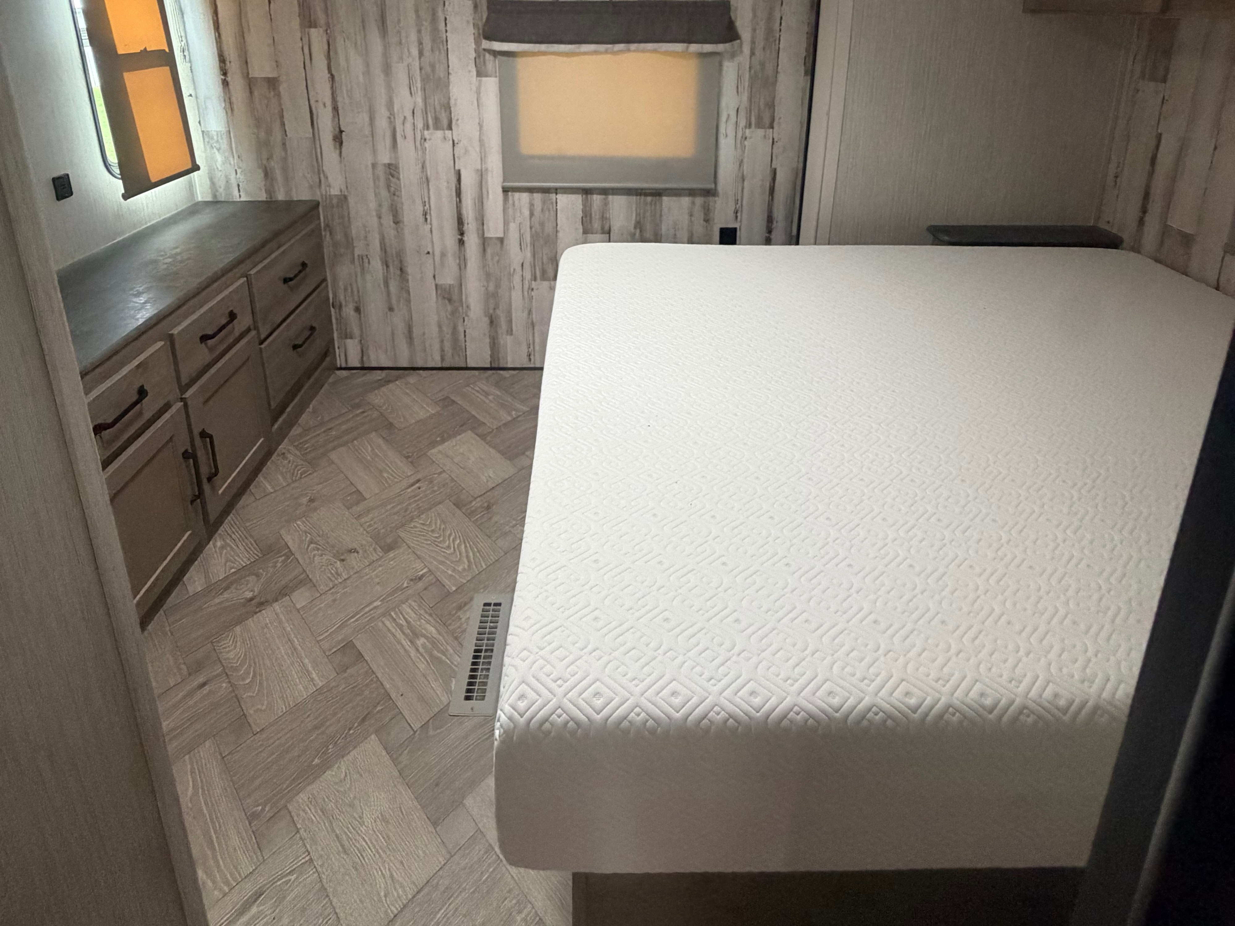 Inside an RV rental bedroom: a clean white mattress, rustic wood-look walls, herringbone flooring, and a dresser.. Forest River Palomino Puma 2021