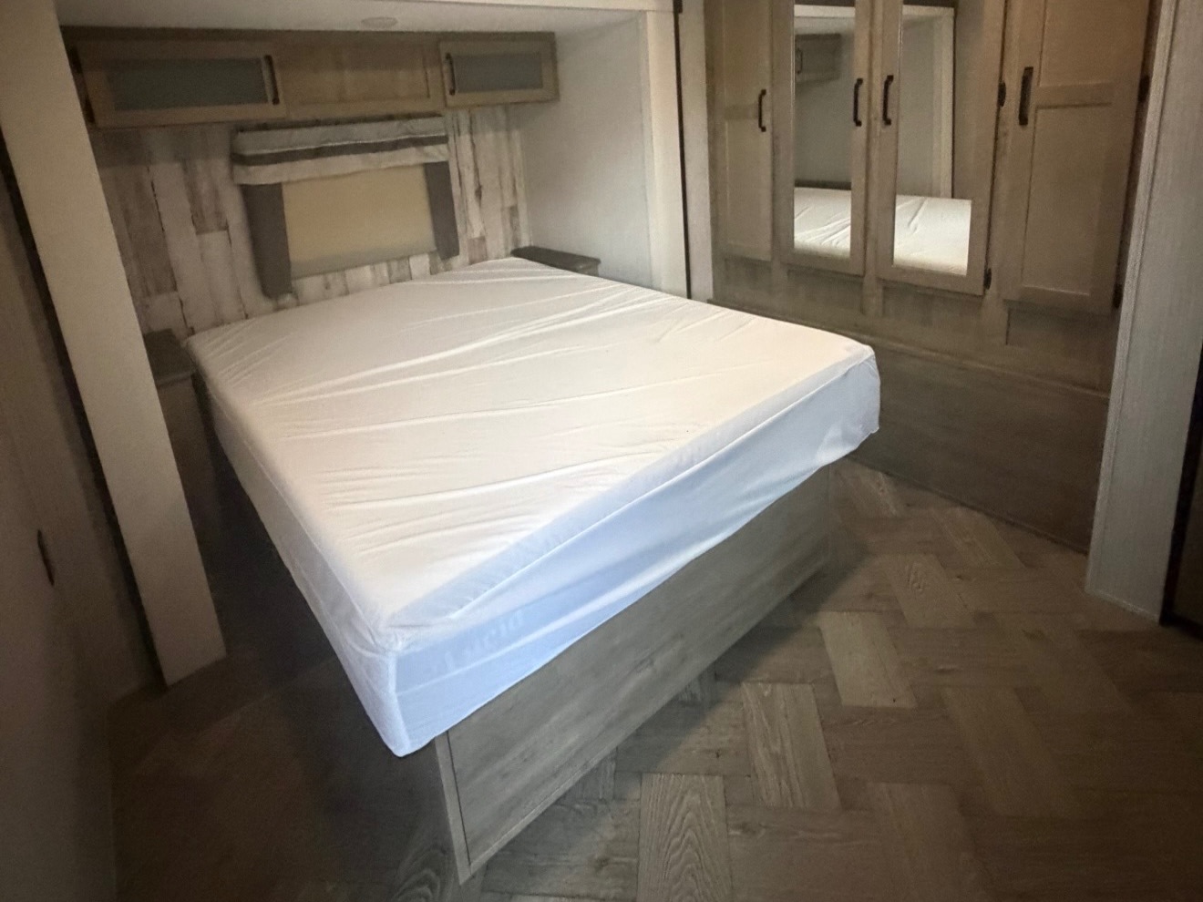 RV rental bedroom with a plastic-covered bed, overhead cabinets, and a mirrored wardrobe, set on wood-look flooring.. Forest River Palomino Puma 2021