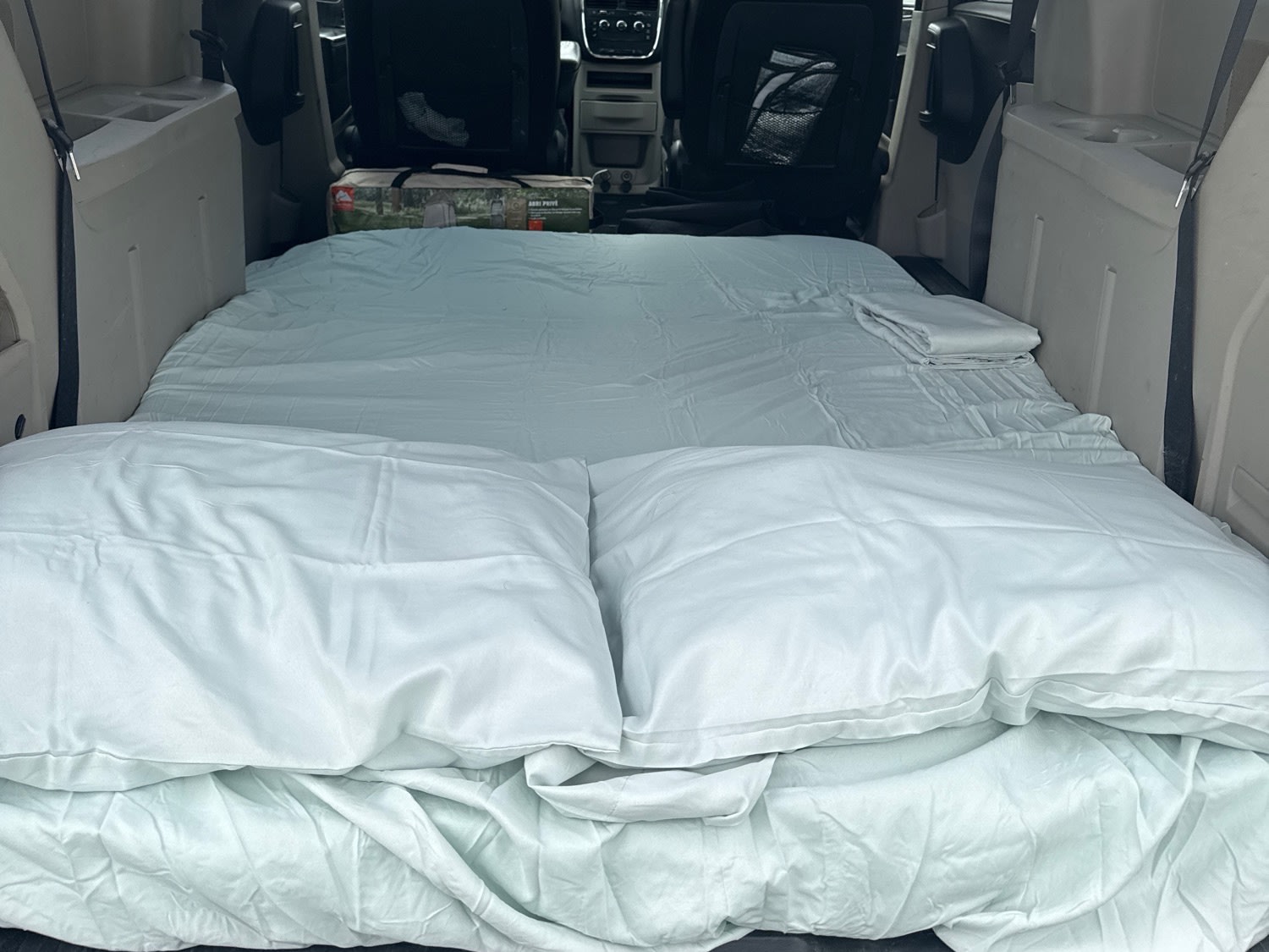 Inside an RV rental, a comfy minivan bed with light blue sheets and pillows, ready for a cozy night's sleep on your road trip.. Dodge Caravan 2014