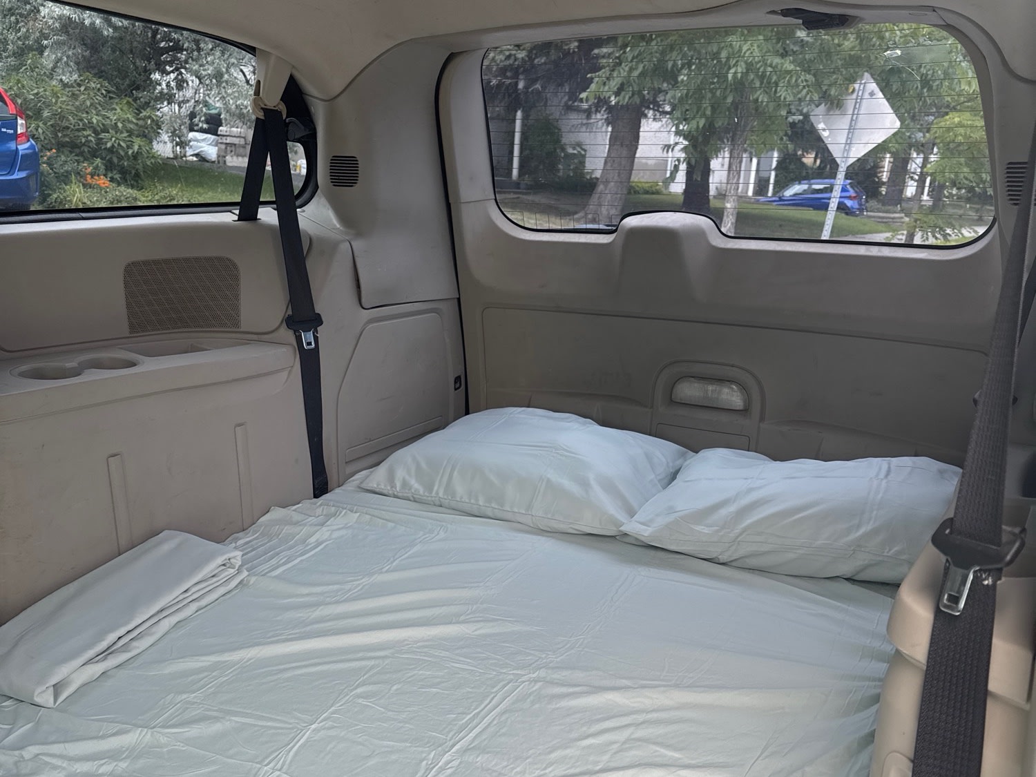 RV rental interior: A comfortable bed with white sheets & two pillows inside a vehicle, ready for camping.. Dodge Caravan 2014