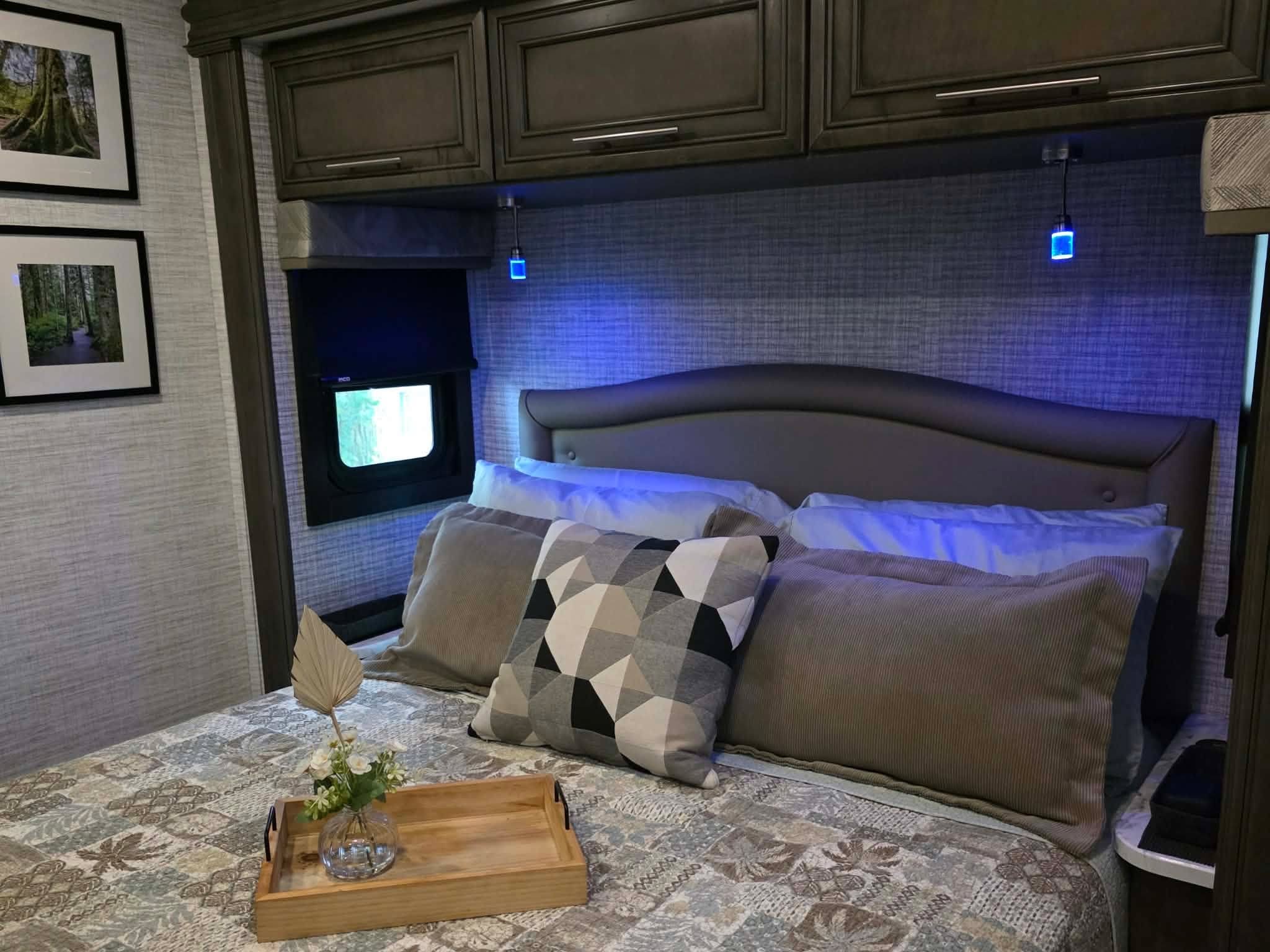 Comfortable RV rental bedroom featuring a patterned bed, cozy pillows, and modern blue accent lighting. Relaxing travel space.. Jayco Greyhawk 2024