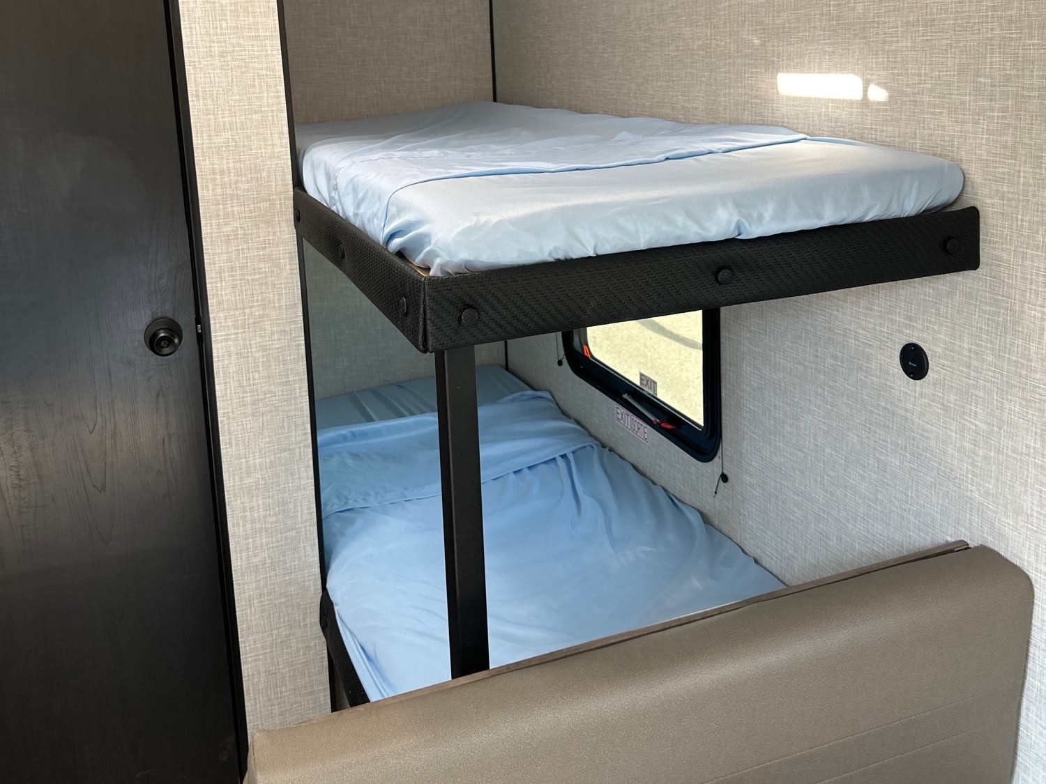 Compact sleeping area in an RV rental, featuring two neatly made bunk beds with blue bedding and a small window.. Highland Ridge RV Open Range Colt Edition 2026