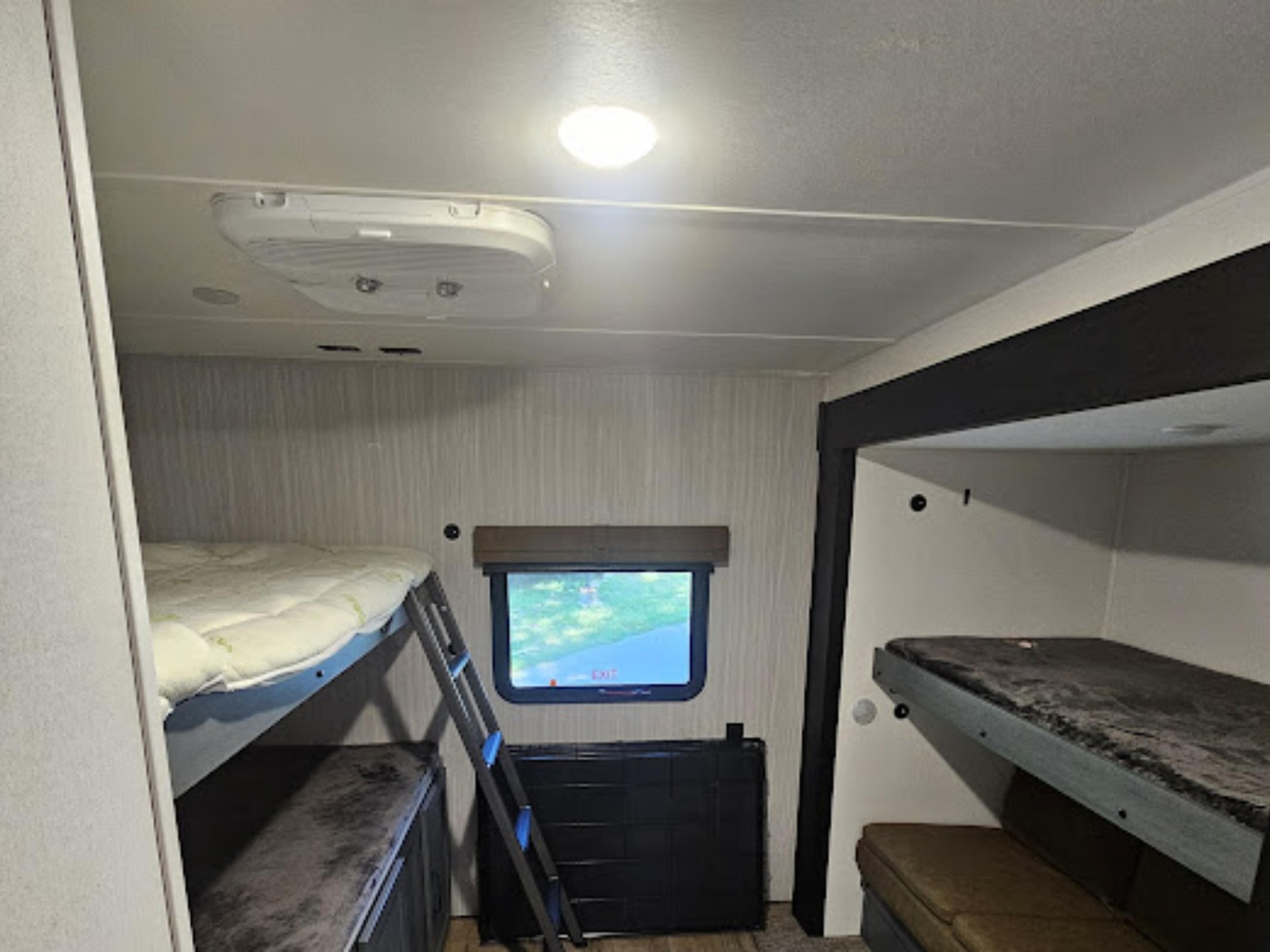 Interior of an RV rental showing two sets of bunk beds, a ladder, window with outside view, and ceiling light and AC unit.. Forest River Palomino Puma 2026