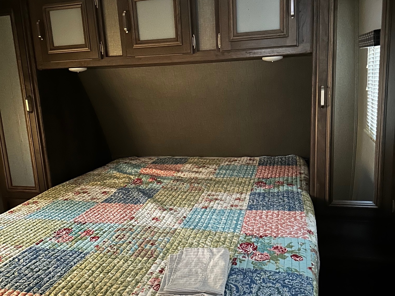 Cozy RV rental bedroom featuring a colorful patchwork quilt, overhead cabinets, and reading lights for comfortable travel.. Keystone RV Passport Grand Touring 2018