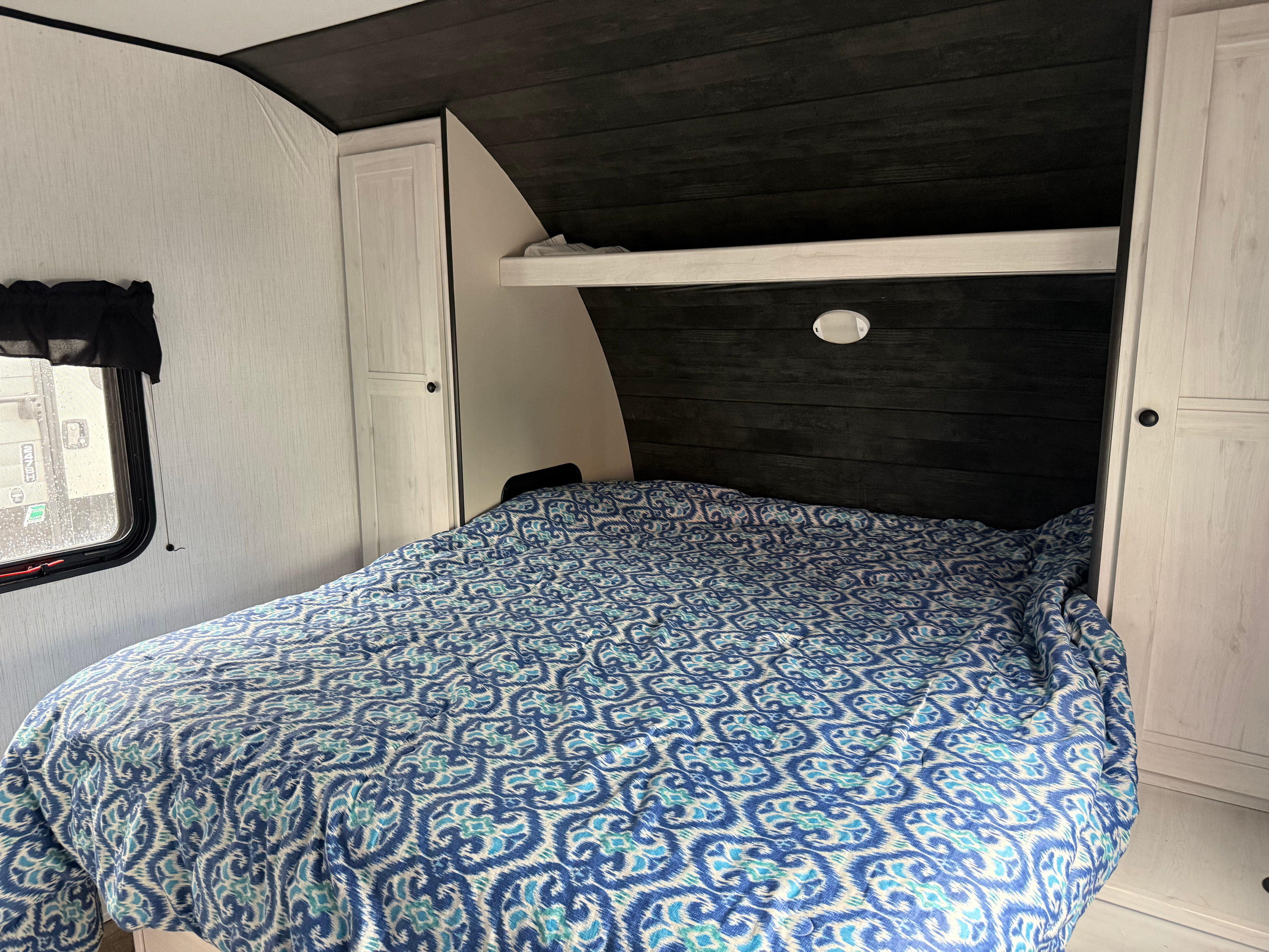 Inside an RV rental, a cozy bedroom featuring a blue patterned bed, dark wood paneling, and white cabinets.. Heartland RVs Trail Runner 2022
