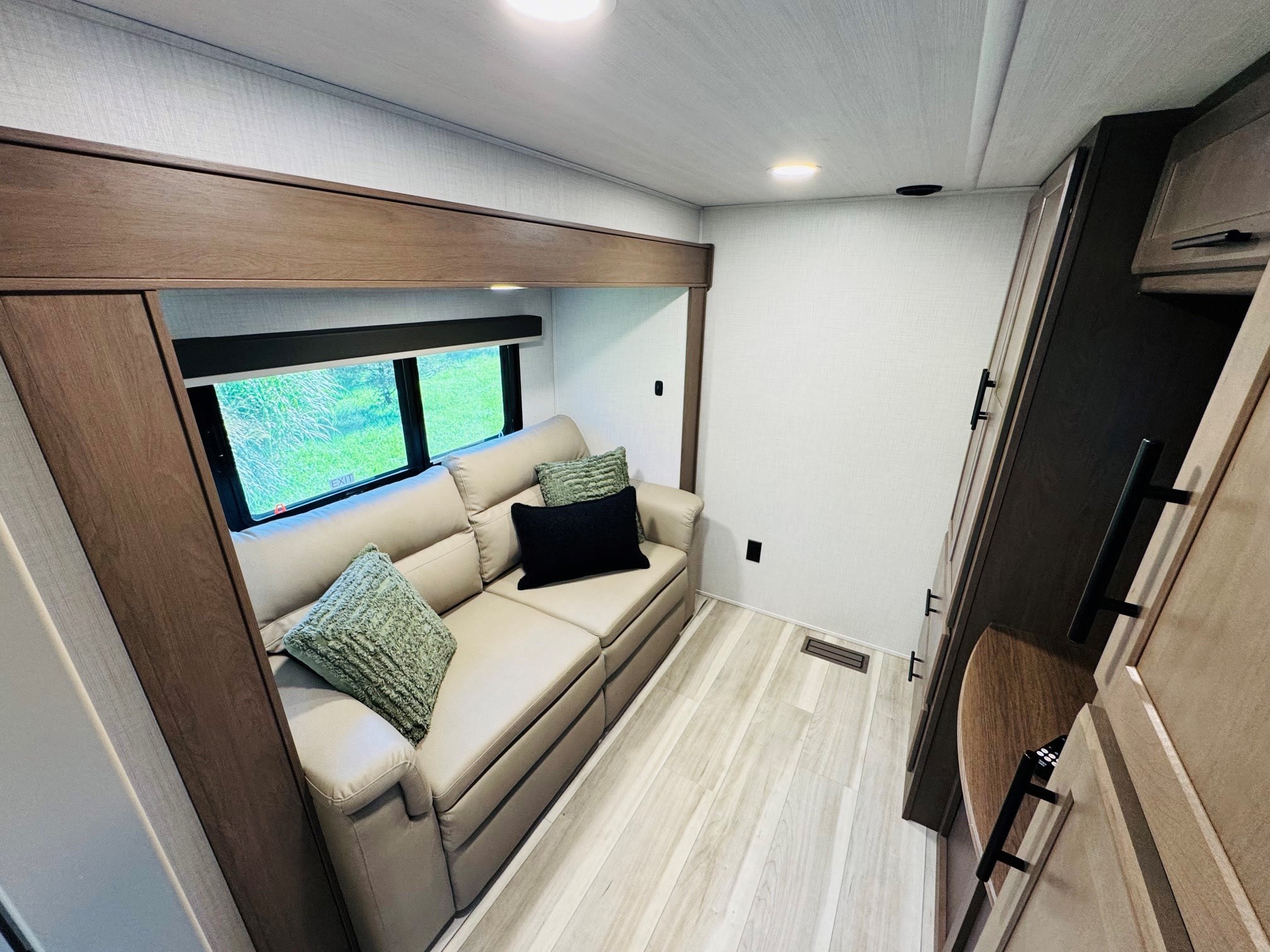 RV rental: Modern interior with a light sofa, green pillows, wood-look floor, overhead storage, and bright window.. Keystone RV Cougar 2026