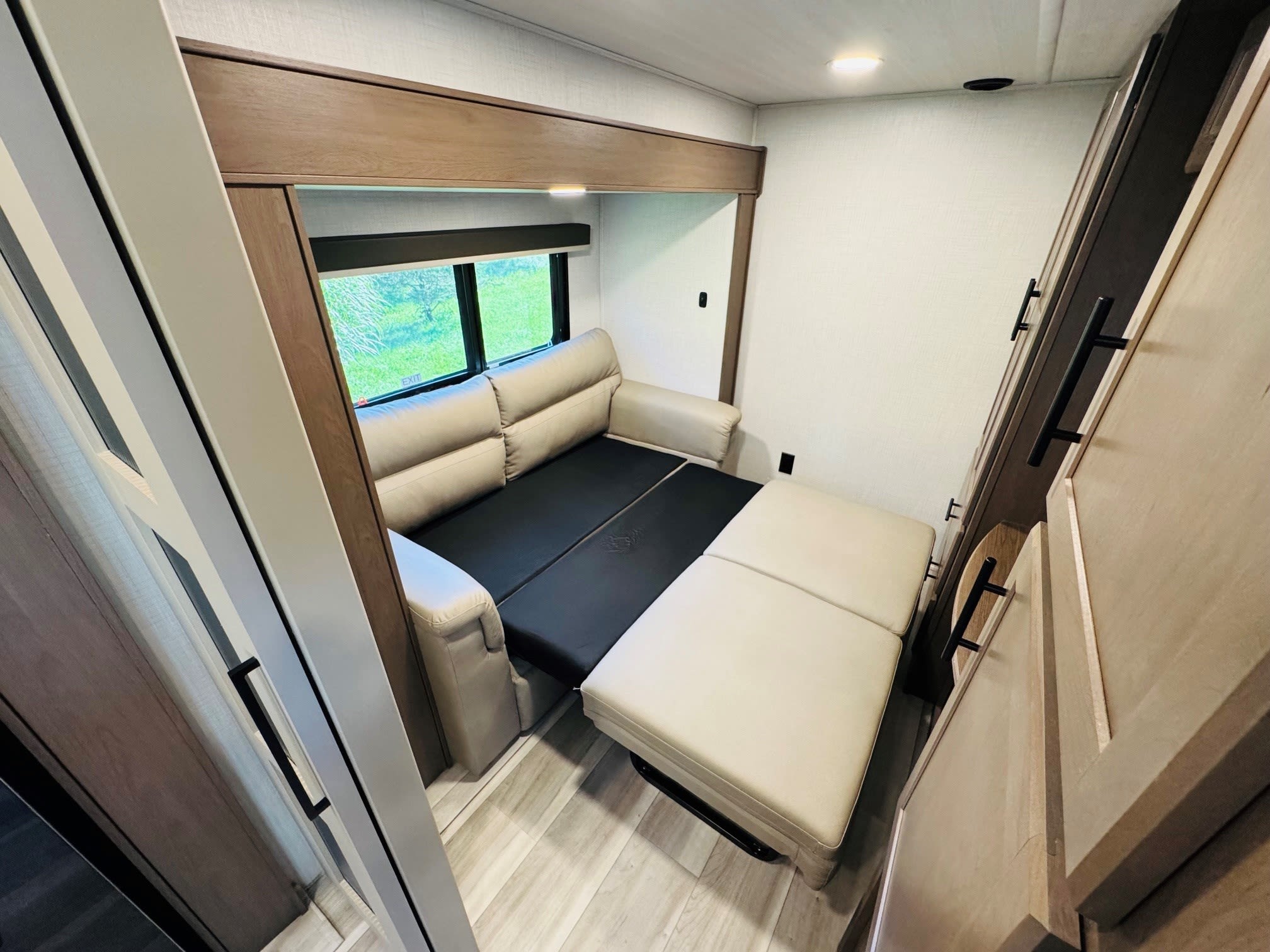 RV rental interior: a convertible sofa bed fully extended, window with nature view, and modern wood cabinetry.. Keystone RV Cougar 2026