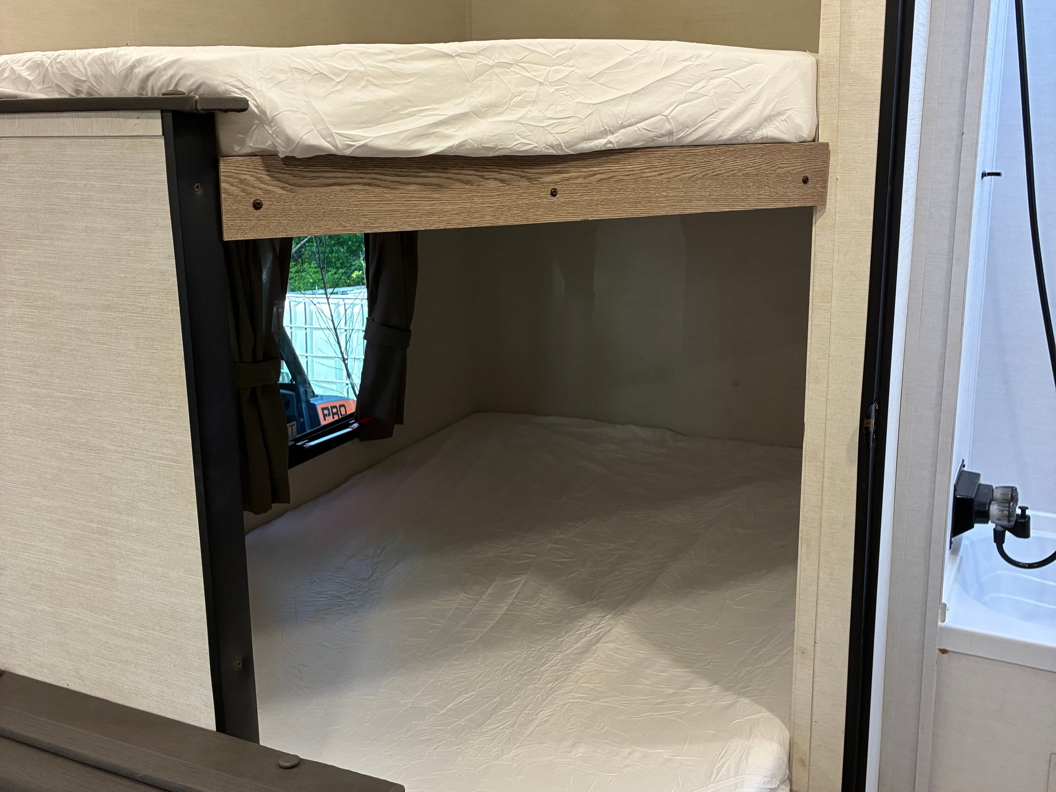 An RV rental's compact interior, featuring bright white bunk beds and a window, ideal for travel adventures.. Gulf Stream Ameri-Lite 2025