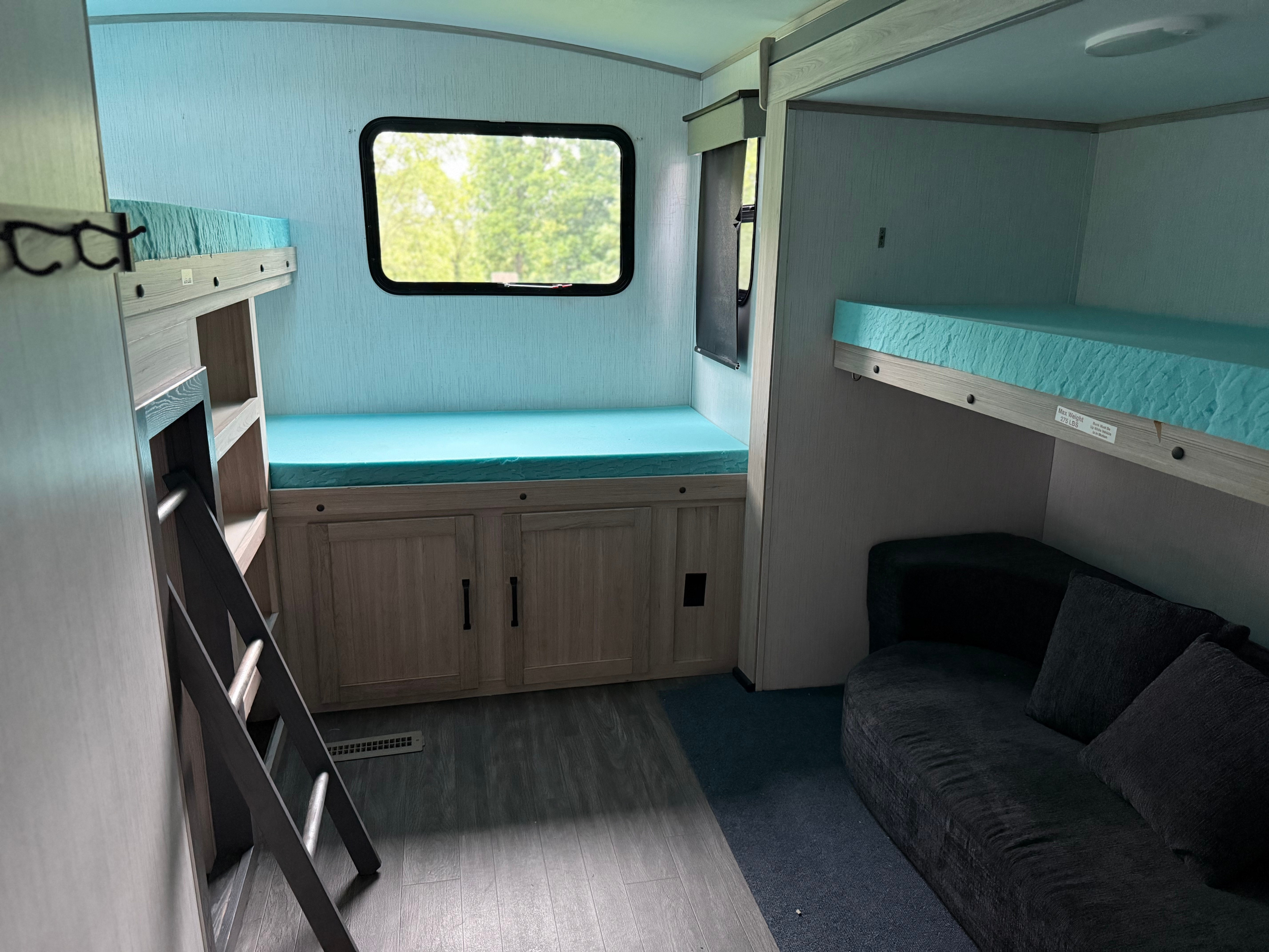 This RV rental bunk room features twin bunk beds with blue mattresses, a ladder, storage cabinets, a window, and a sofa.. Twilight RVS Signature 2022