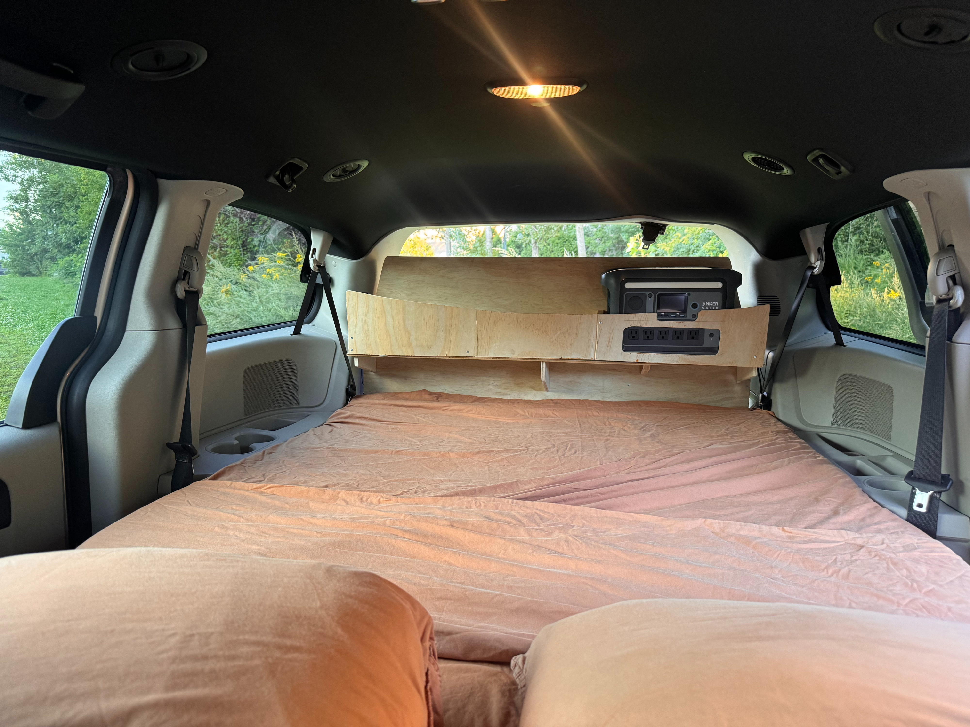 Inside an RV rental: a minivan converted with a comfortable bed, wood shelving, and a portable power station for car camping.. Dodge Grand Caravan 2015