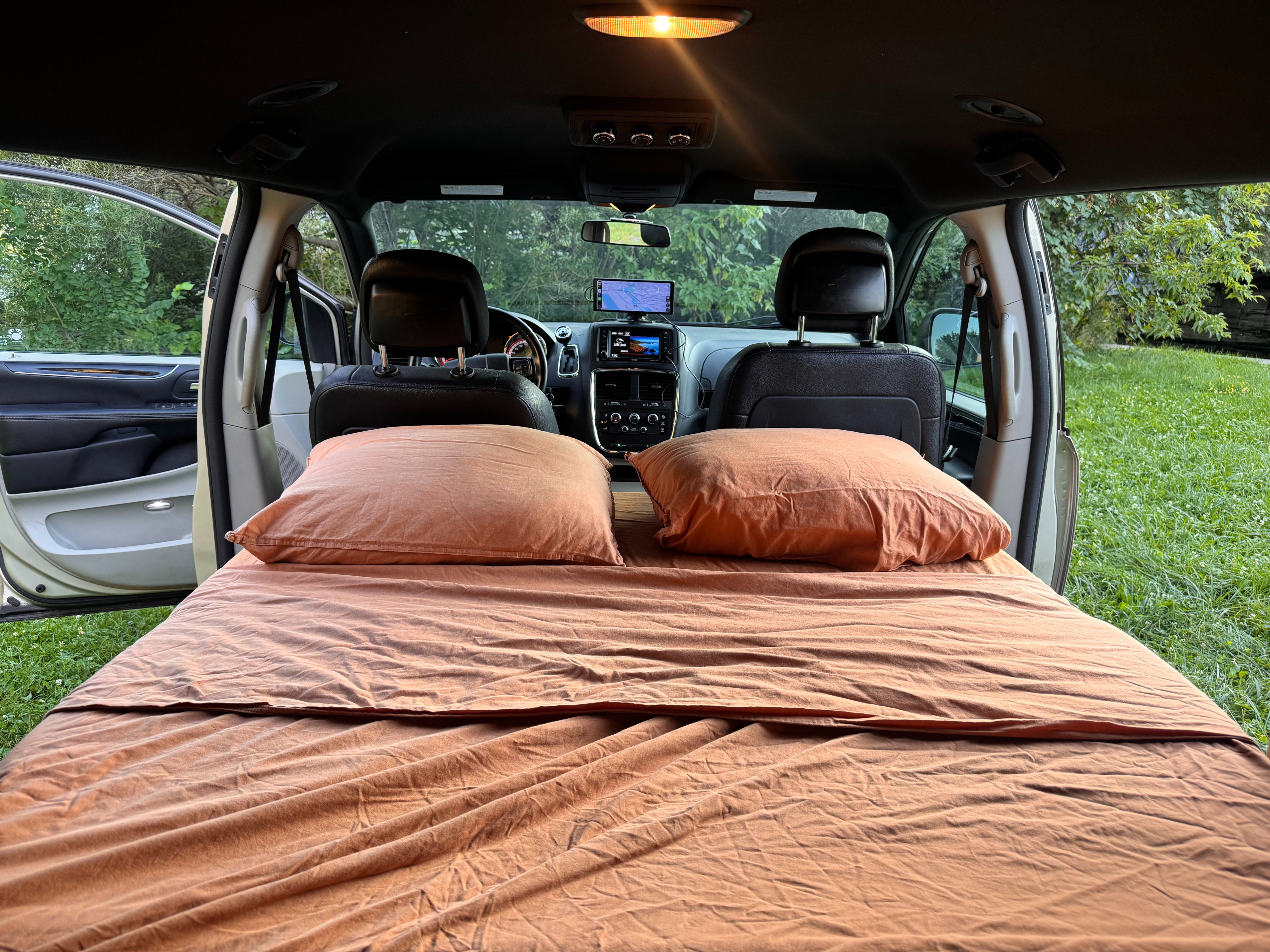 Minivan rv rental: converted interior with a comfy bed, front cabin, and open doors to green outdoors.. Dodge Grand Caravan 2015