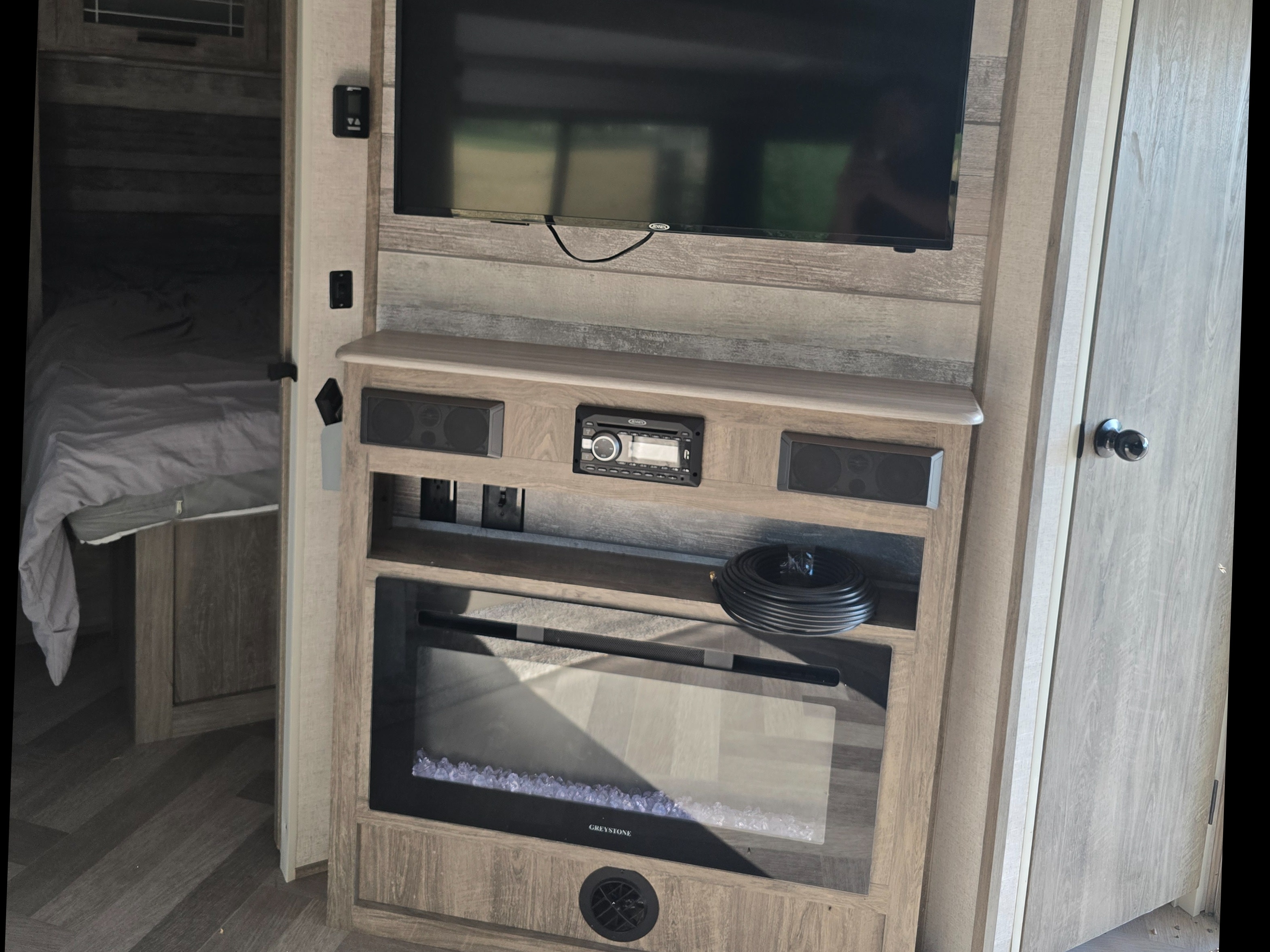 Modern RV rental interior with an entertainment center featuring a TV, stereo, electric fireplace, and a bedroom visible.. Forest River Salem Hemisphere HL 2021