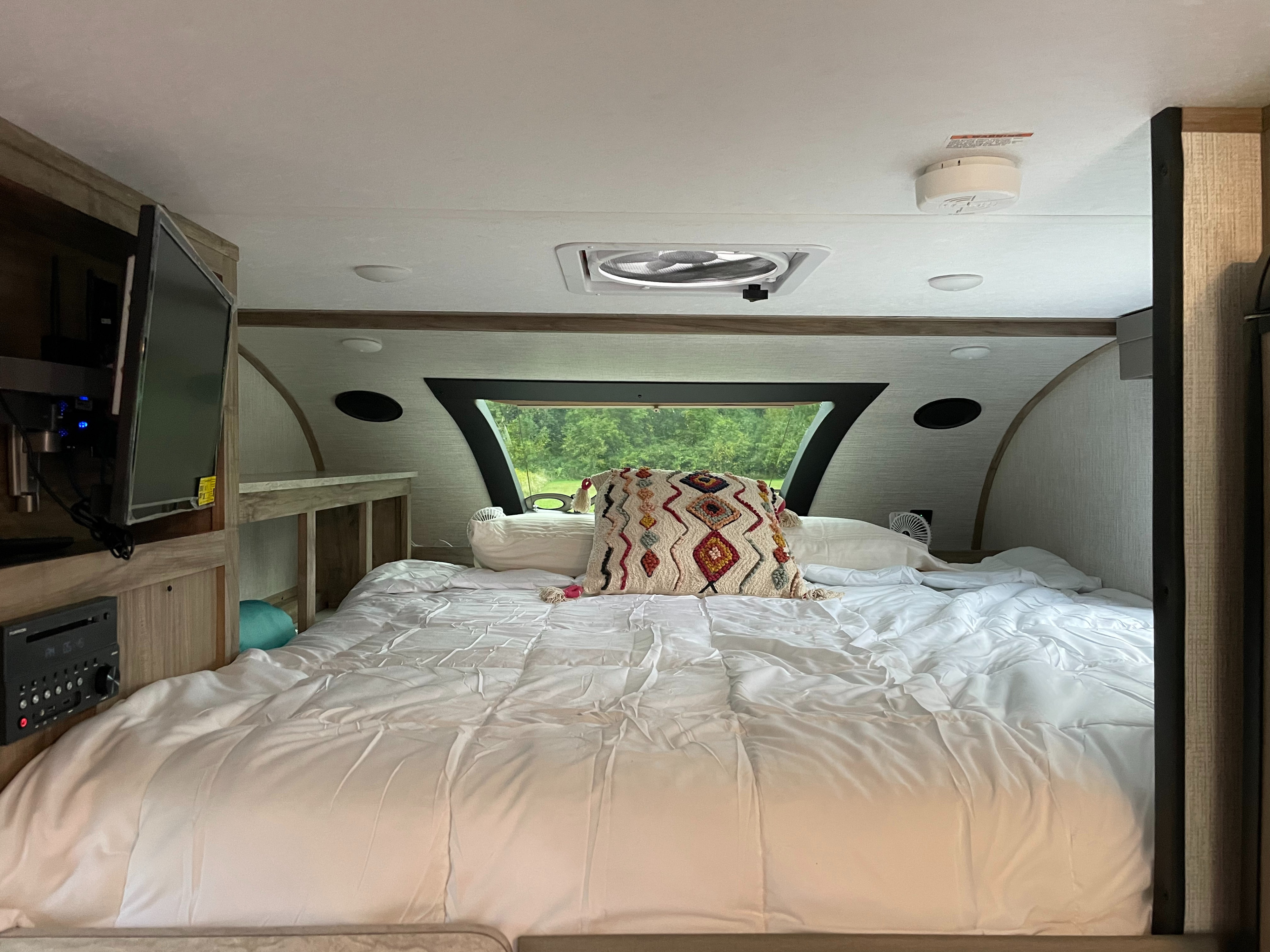 Relaxing RV rental bedroom showing a comfy bed with white linens, a TV, and a large window with a lush green view outside.. Palomino Backpack Edition 2023