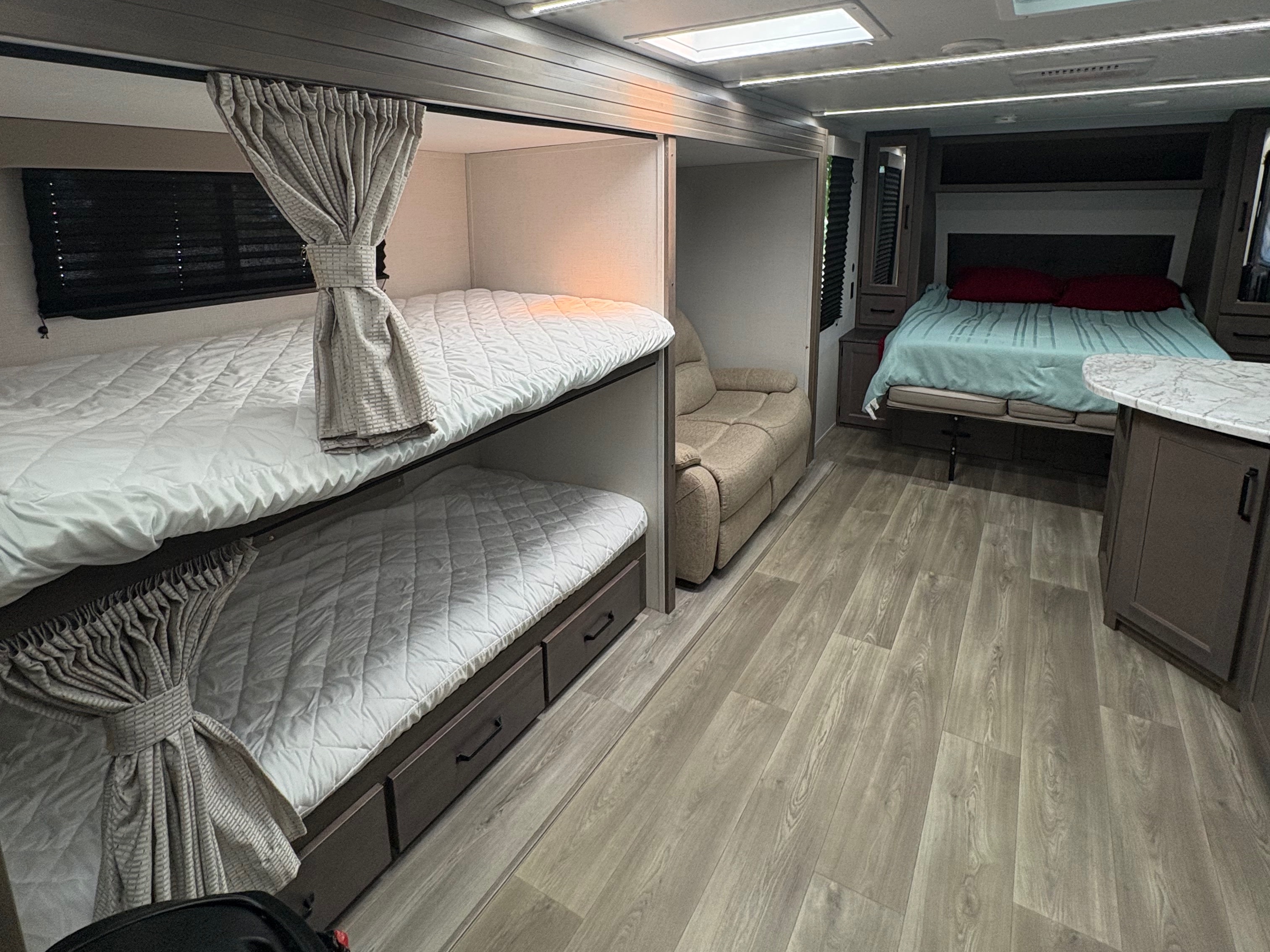 Spacious RV rental interior with bunk beds, master bed, recliner, and wood-look floors, perfect for a comfortable getaway.. Grand Design Transcend Xplor 2024