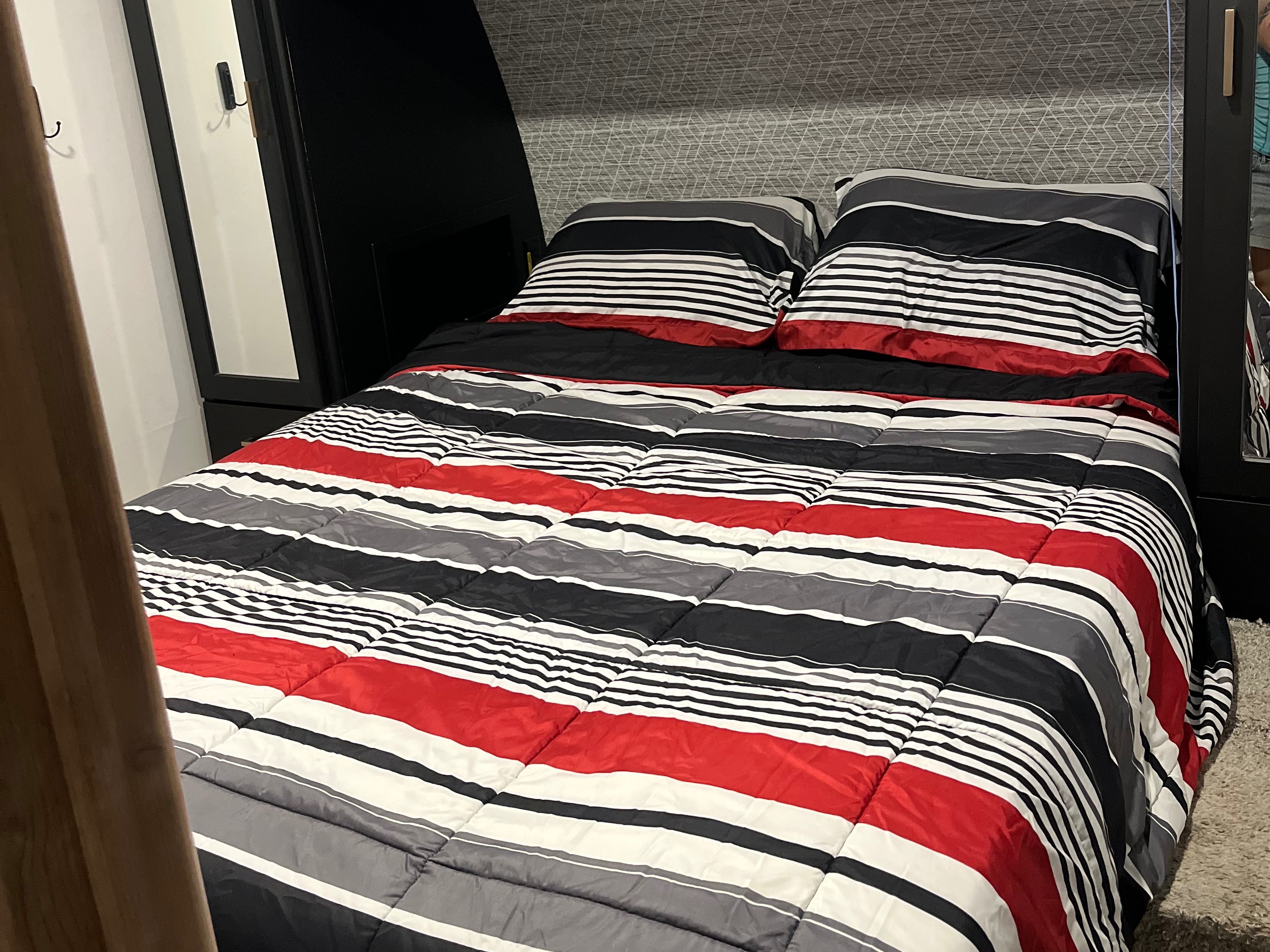 Cozy bed in an RV rental bedroom, featuring a vibrant red, black, white, and gray striped comforter and pillows.. Keystone RV Outback 2022