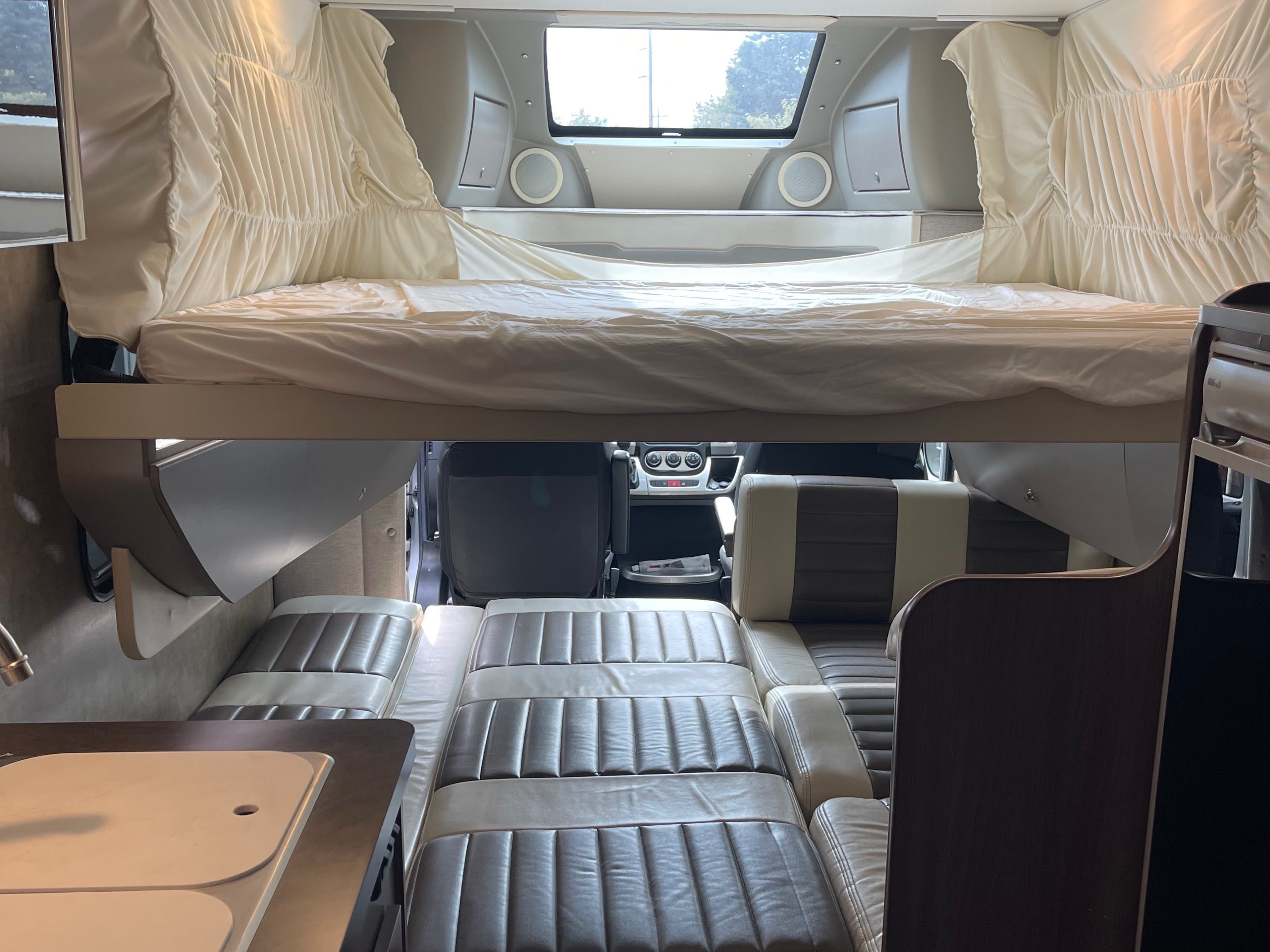 Comfortable rv rental interior featuring an elevated bed, convertible lounge, and compact kitchen for travel adventures.. Winnebago Trend 2015