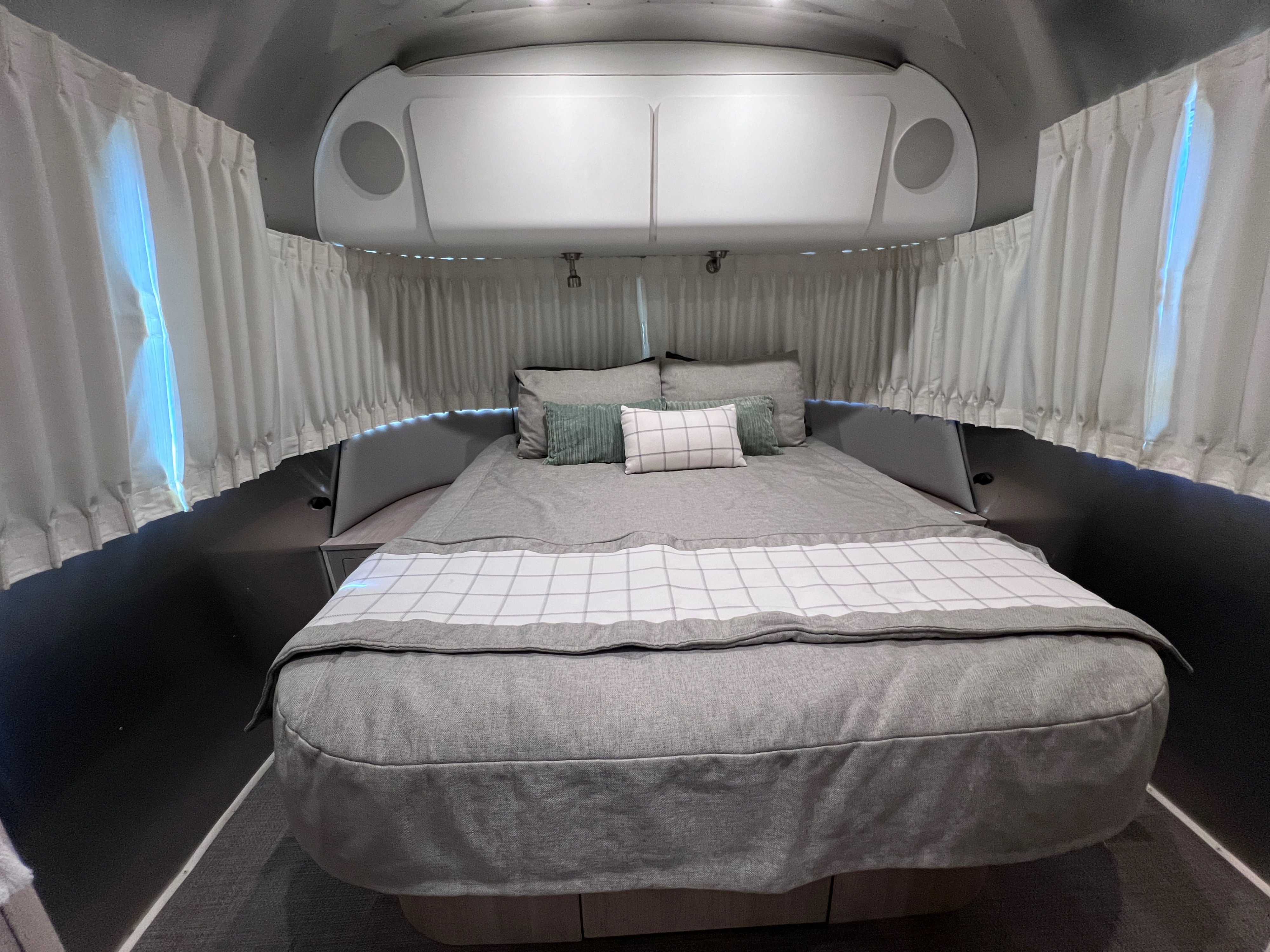 Cozy RV rental bedroom with a comfy bed, modern grey decor, white curtains, and overhead storage, perfect for travel.. Airstream Globetrotter 2022