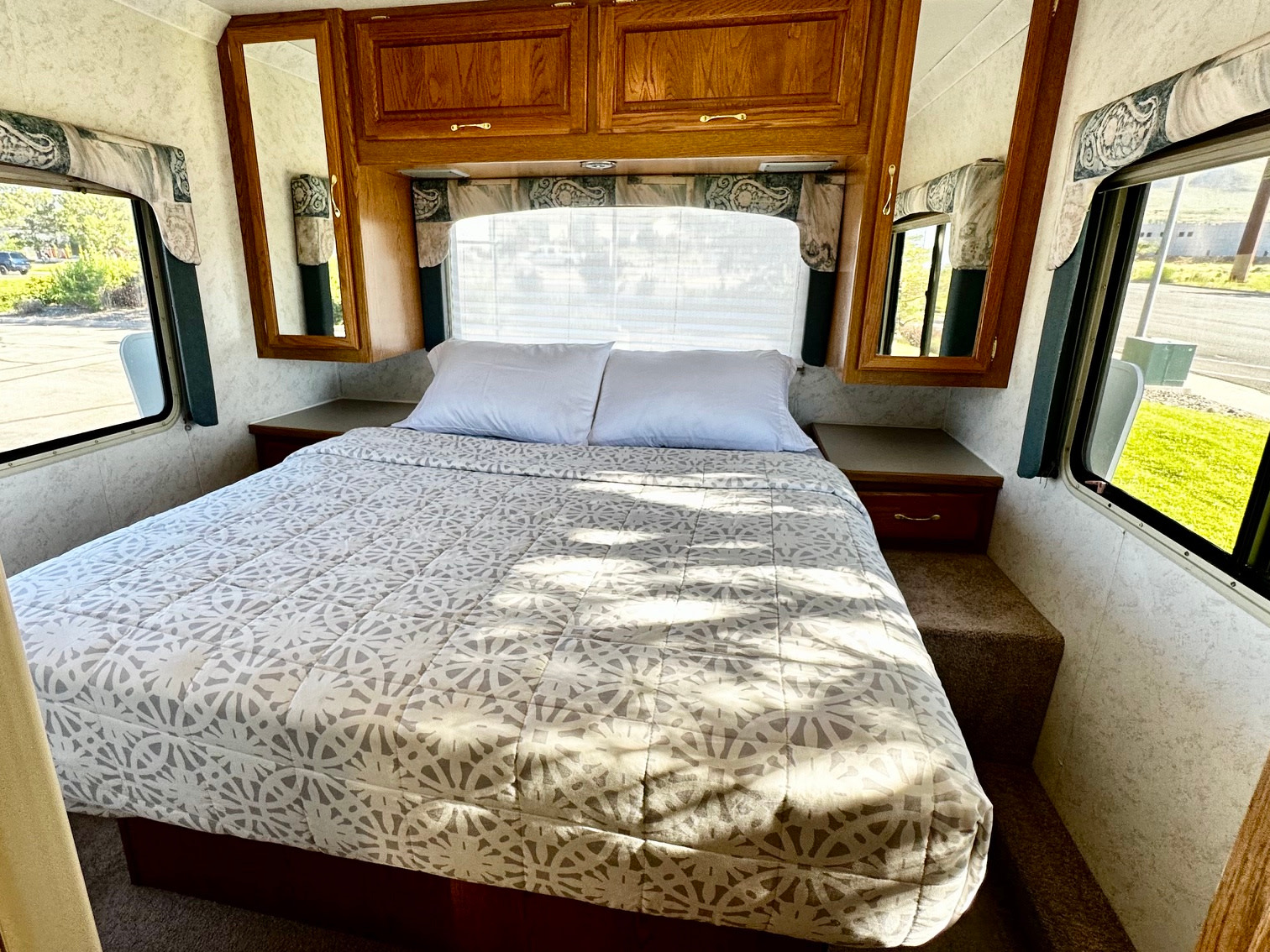 Comfortable RV rental bedroom with spacious bed, windows, and storage. Bright interior for your adventure.. Four Winds Hurricane 2002