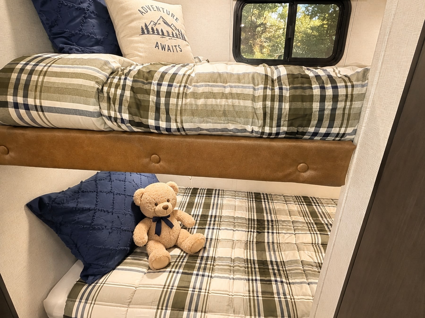 This RV rental features cozy bunk beds with plaid bedding, an "Adventure Awaits" pillow, and a teddy bear, perfect for family trips.. Keystone Springdale West BHWE 2025