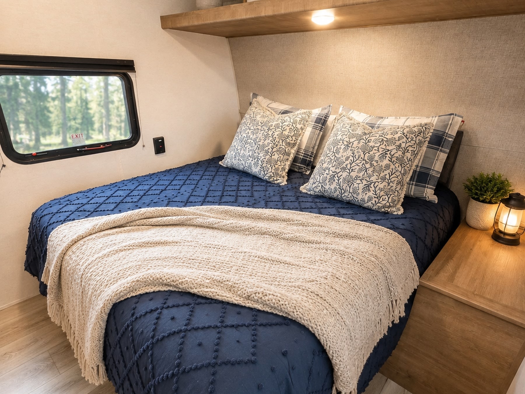 Experience comfort in this cozy RV rental bedroom. Features a plush bed with blue quilt, window view, and lantern on nightstand.. Keystone Springdale West BHWE 2025