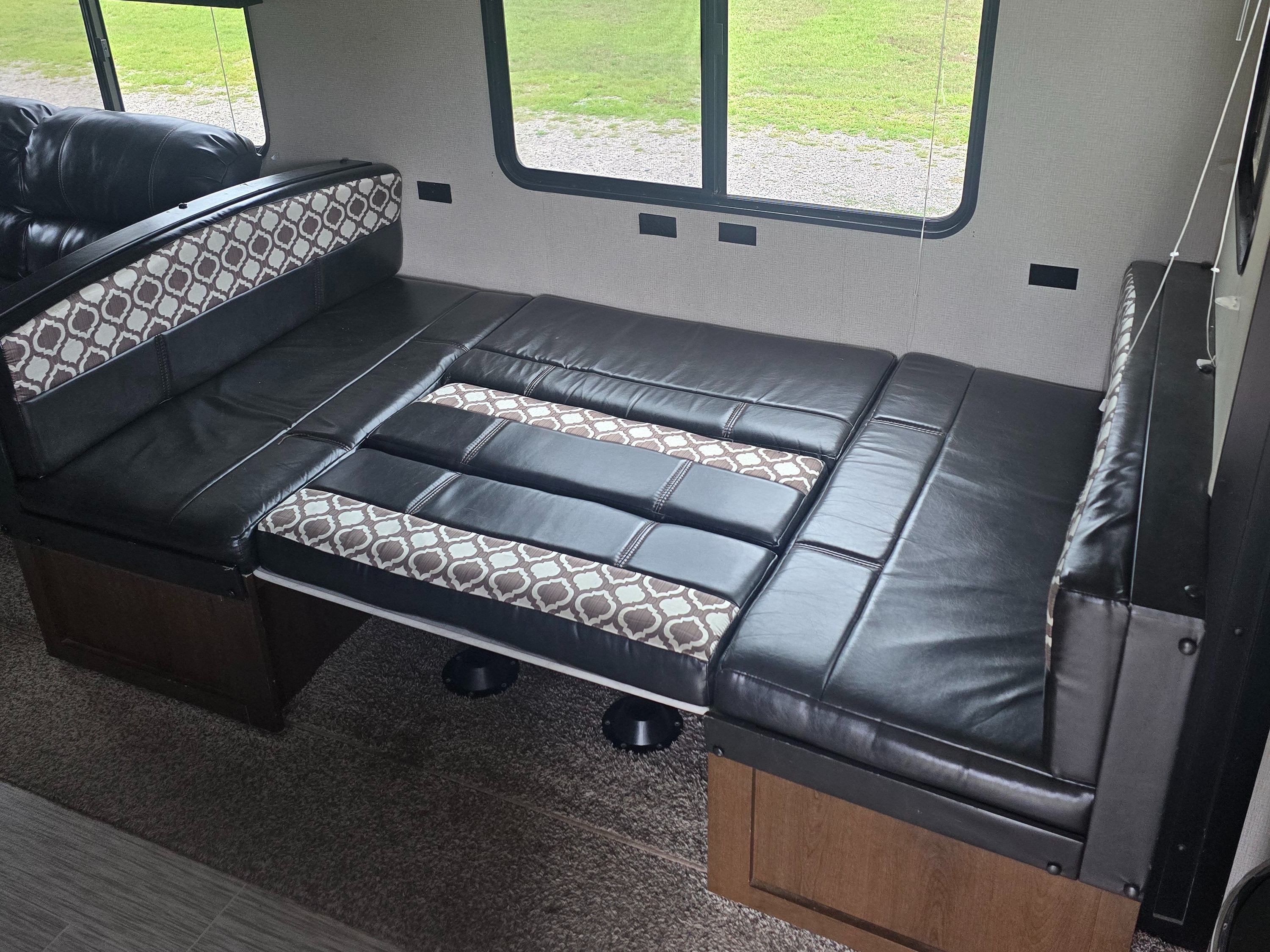 RV rental dinette converted into a comfy bed with black leather and patterned cushions, offering a cozy sleep space inside.. Avenger ATI 2018