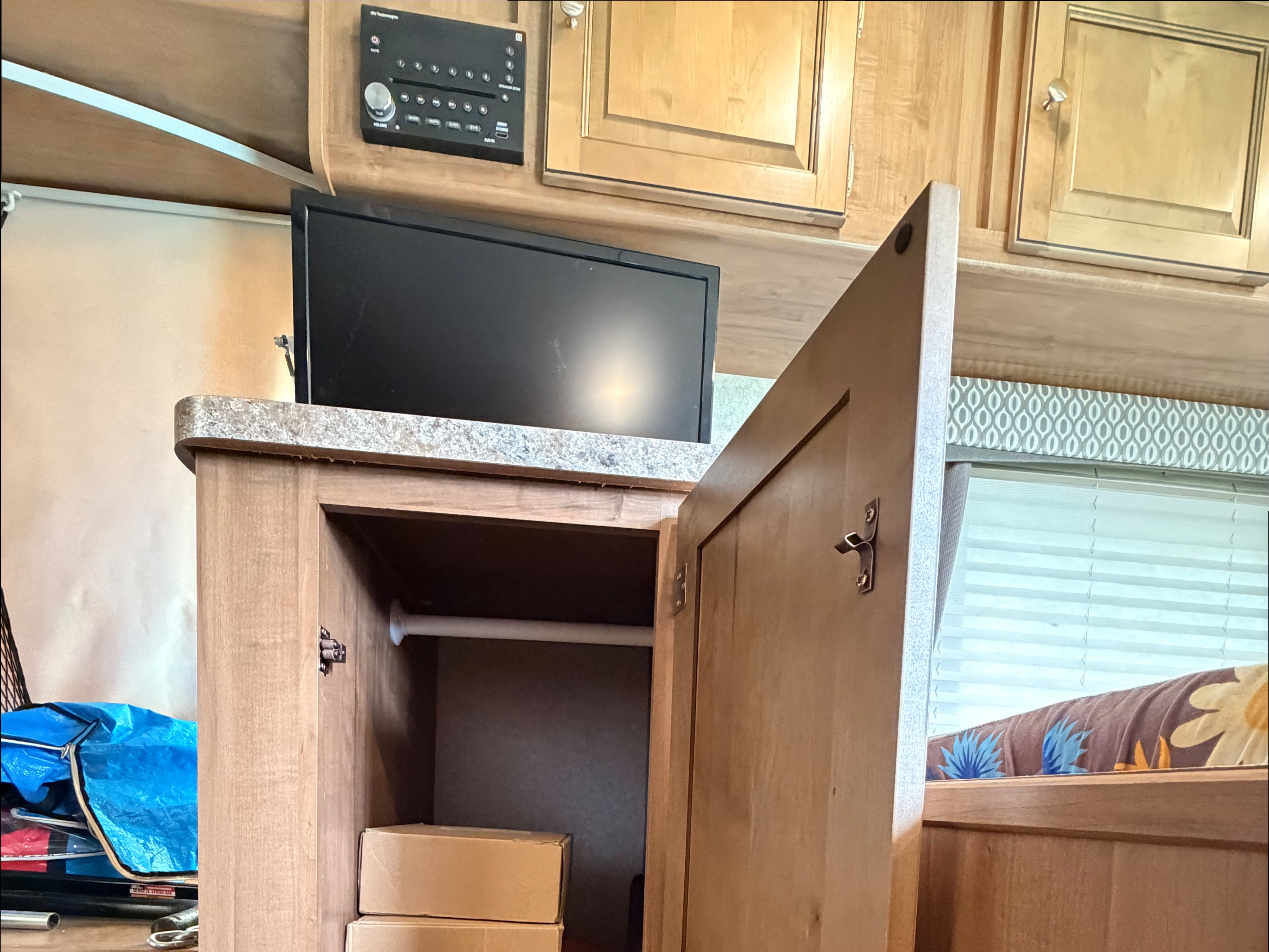 Inside an RV rental: wood cabinets, TV, audio panel, open closet with boxes, and window with blinds.. Forest River Flagstaff Shamrock 2018