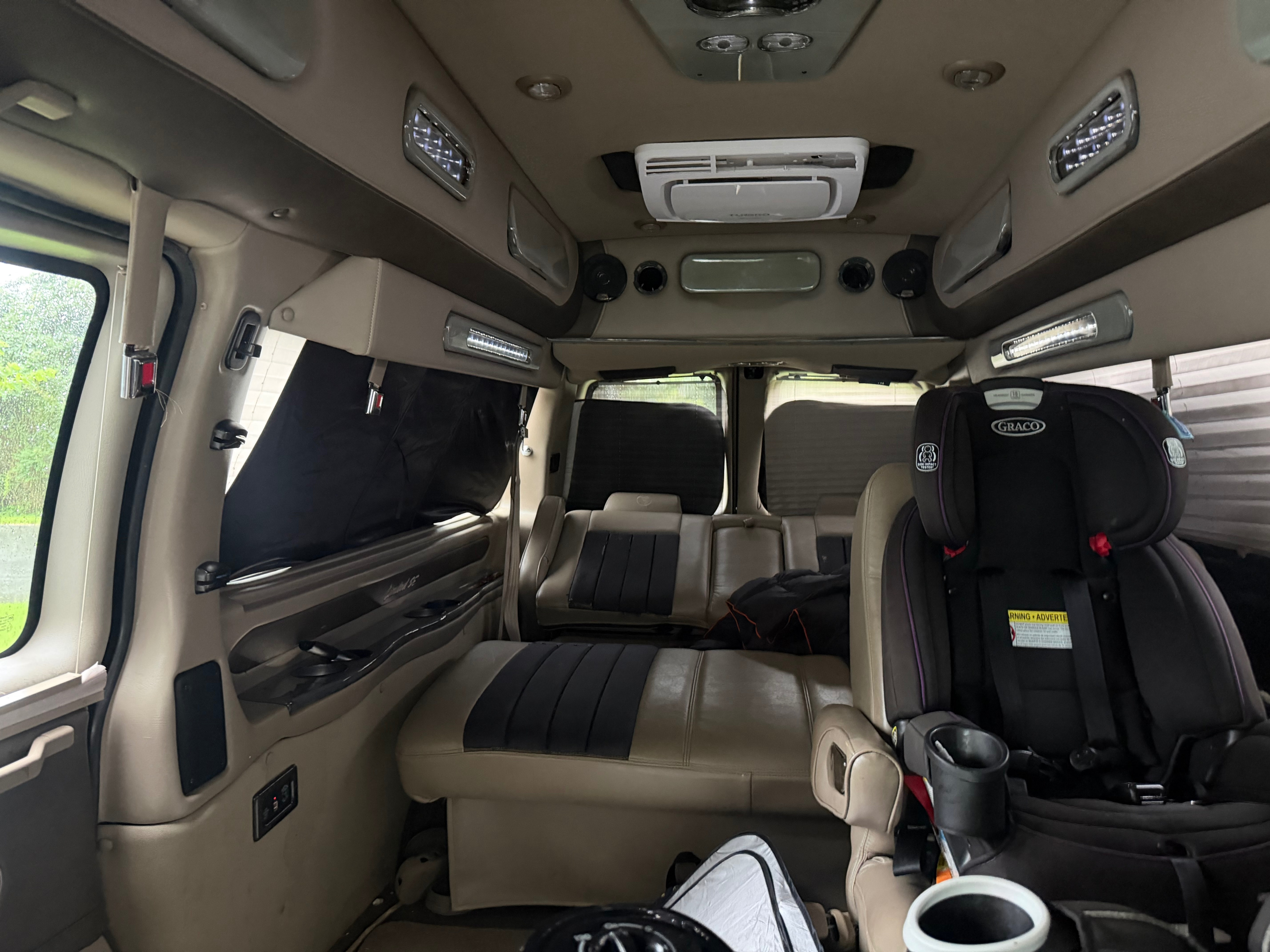 Inside a custom RV rental: family seating, child car seat, bed, and overhead AC/lighting for comfortable travels.. Chevrolet Explorer 2014