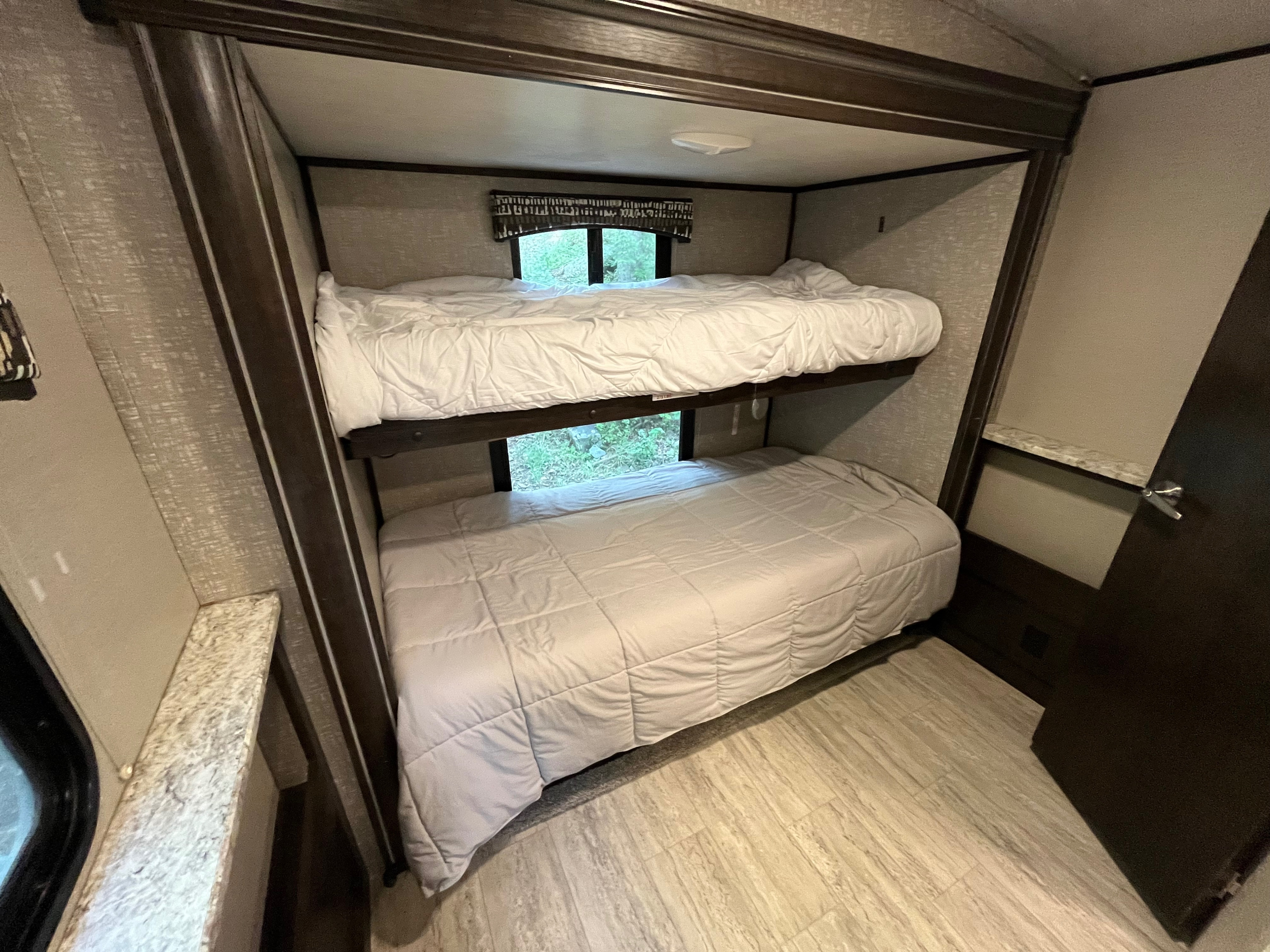 Spacious RV rental bunk beds with clean white comforters and windows revealing nature. A cozy camper interior for family sleeping.. Cruiser RV Shadow Cruiser 2018